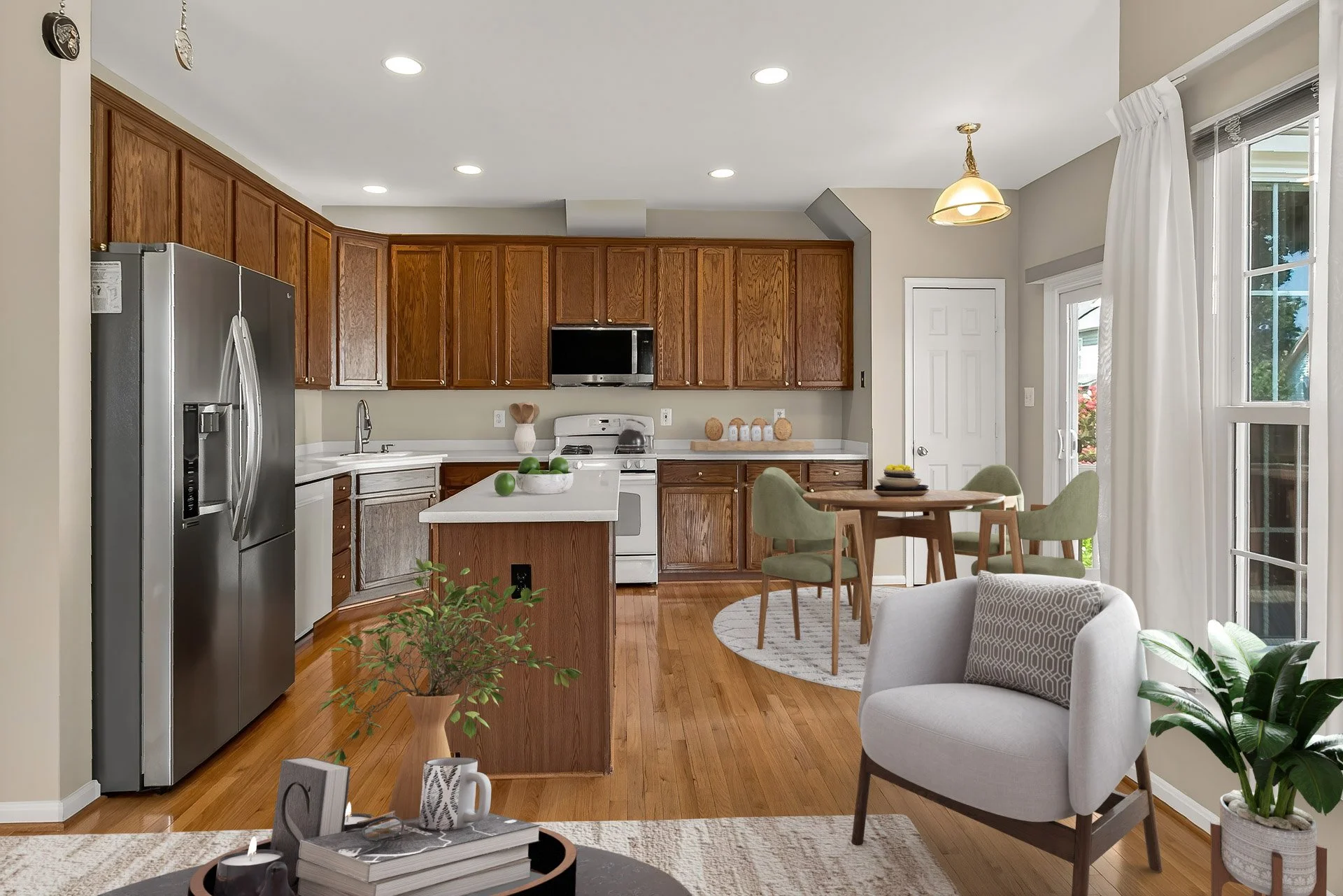 Open kitchen with wooden cabinets, stainless steel refrigerator, white countertops, and a dining area with a round table and four green chairs. A white armchair and potted plant are visible in the foreground.