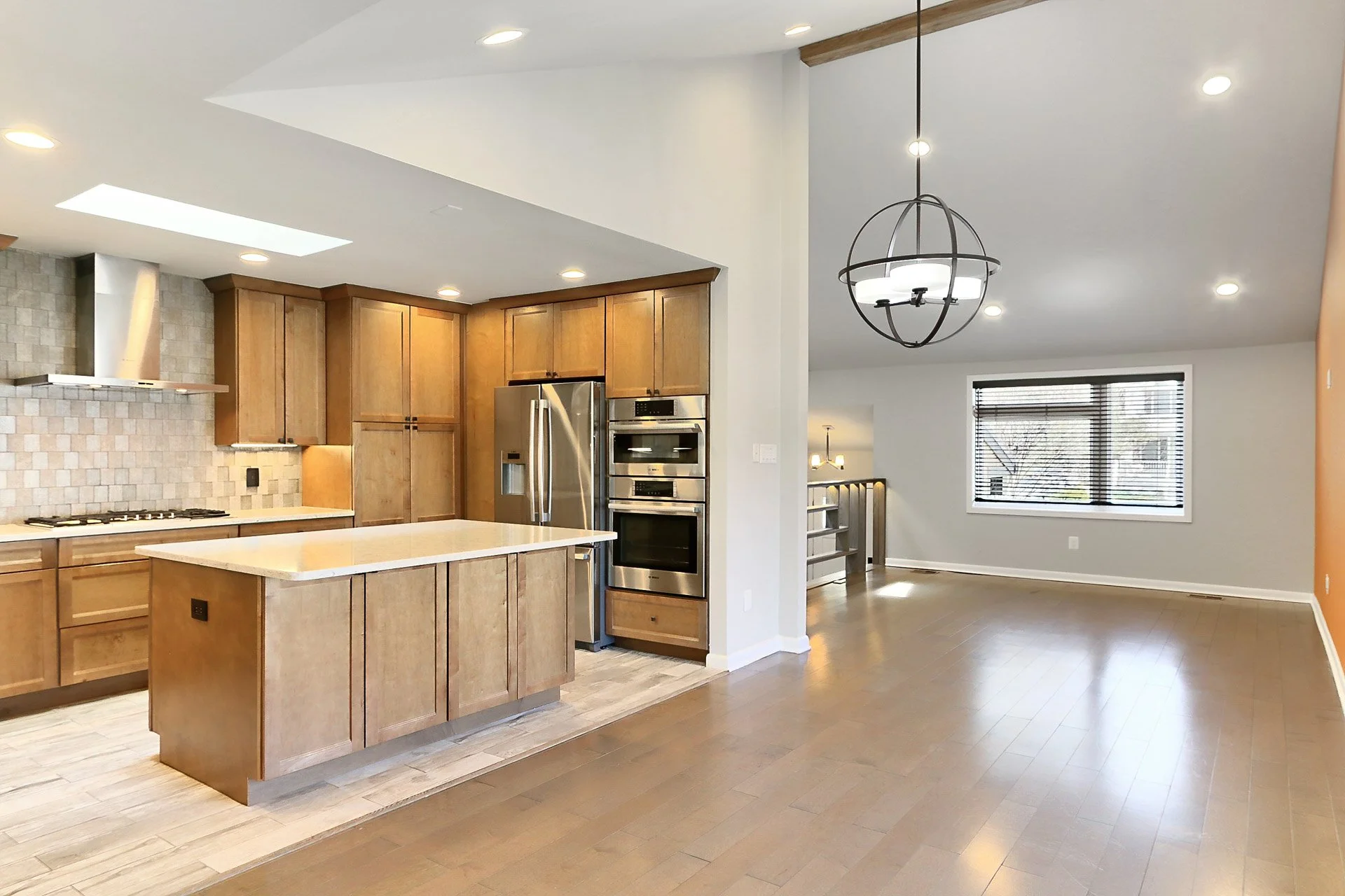 Open-concept kitchen and dining area with wooden cabinets, stainless steel appliances, a central island, hardwood floors, and large windows letting in natural light.
