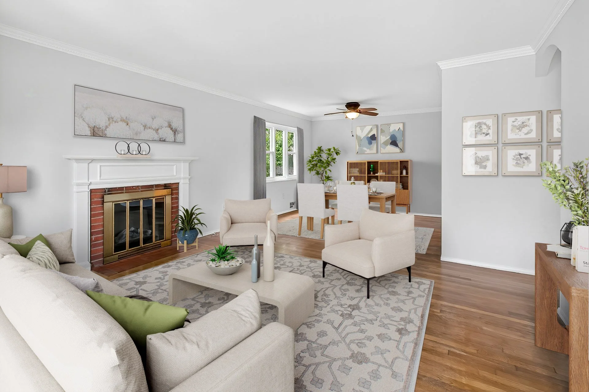 Cozy living room with white walls, hardwood floors, a fireplace, beige seating, a coffee table with decorative vases, and a dining area with a wooden table and white chairs in the background.
