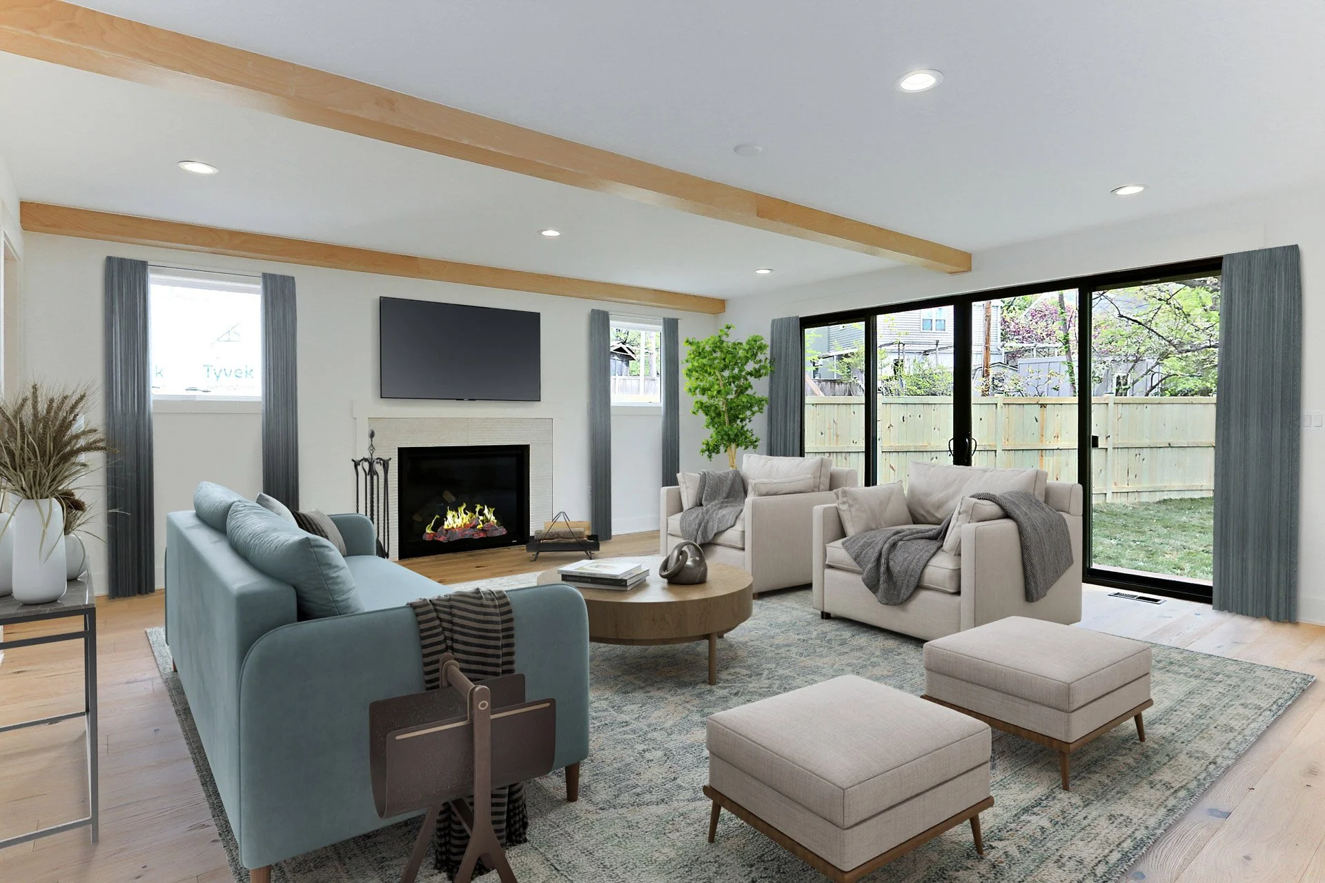 Living room with a fireplace, wall-mounted TV, blue and white sofas, a wooden coffee table, ottomans, indoor plants, and large sliding glass doors leading to a backyard