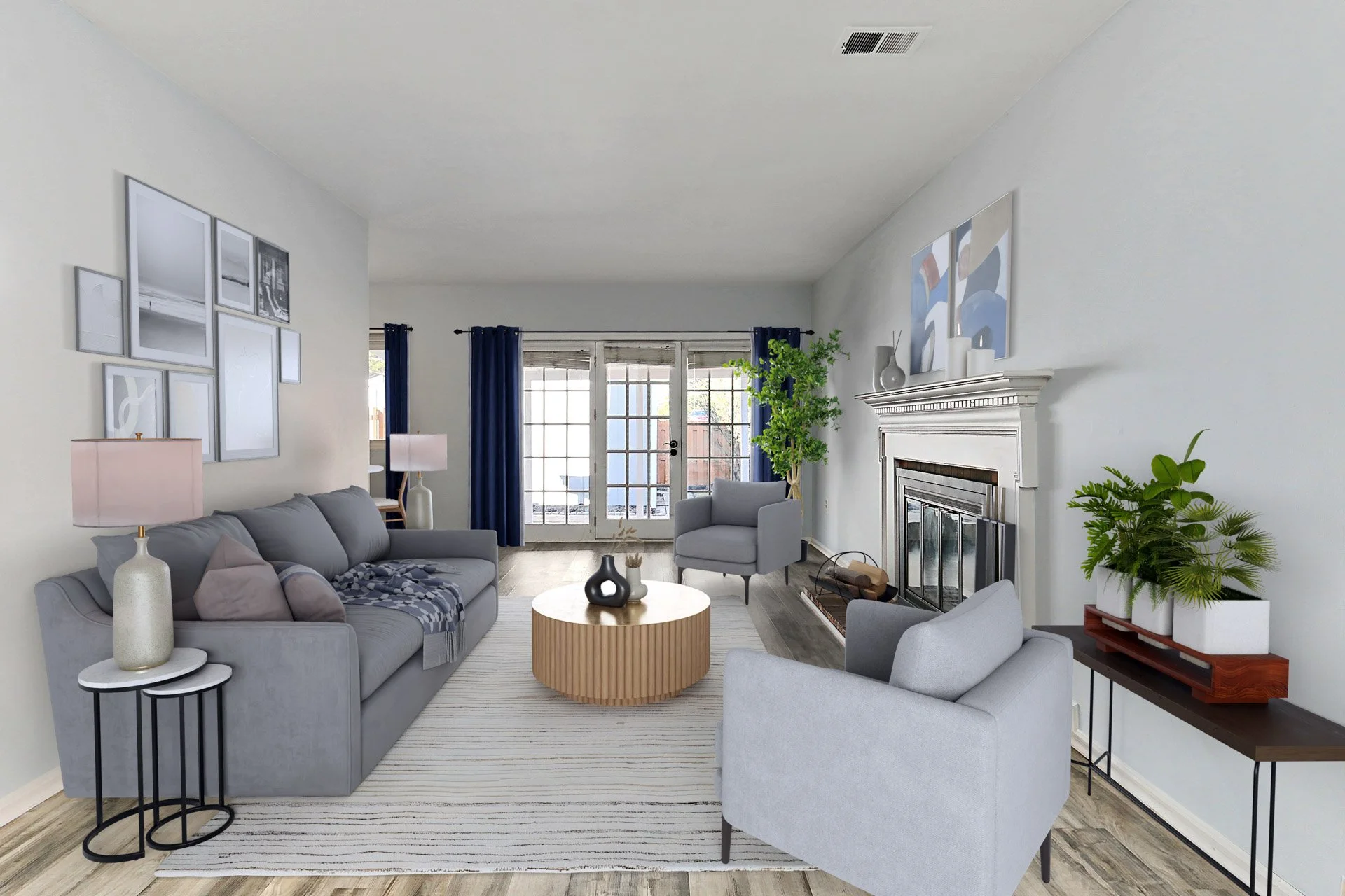 Living room with gray sofa, two gray armchairs, a round wooden coffee table, potted plants, a fireplace, and artwork on the walls, with large glass doors and dark blue curtains.
