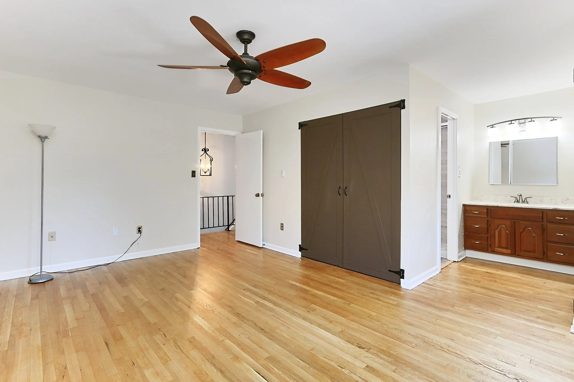 Living room with hardwood floor, ceiling fan, free-standing lamp, sliding barn door, and a bathroom vanity with a mirror.