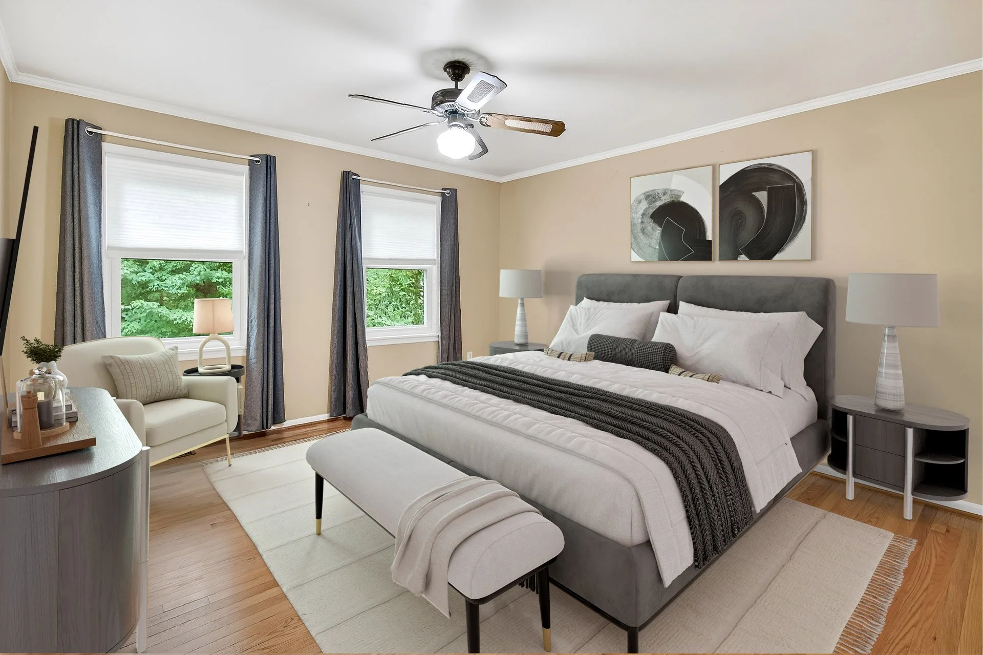 A modern bedroom with a large bed, dark gray headboard, white bedding, black blanket, and decorative pillows. There are two side tables with white lamps, a bench at the foot of the bed, a beige armchair with a cushion, and two windows with dark curta