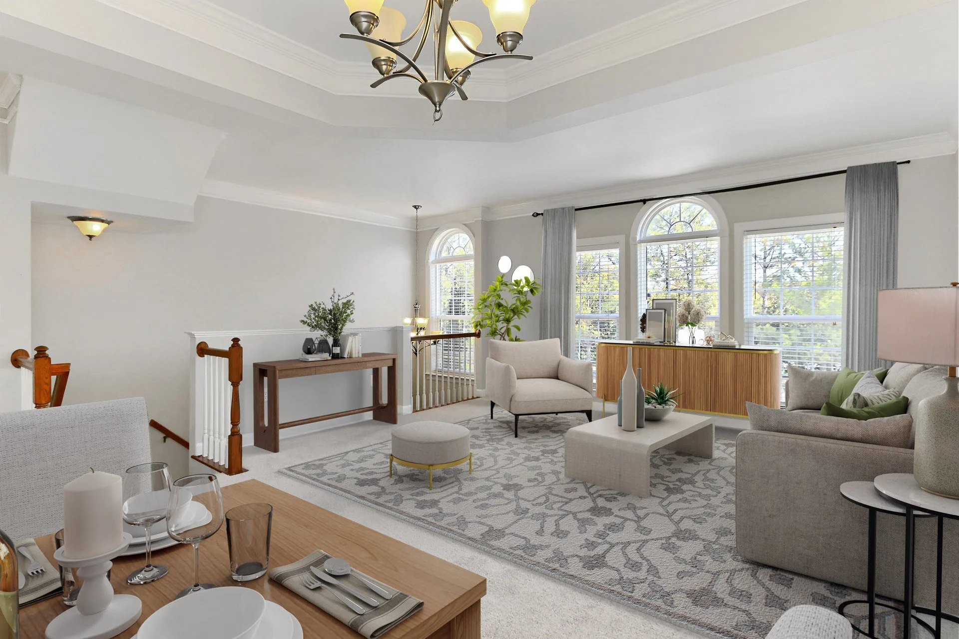 Bright living room with large arched windows, white walls, and modern furniture including sofas, armchair, and coffee table with decorative vases and plants, illuminated by a large chandelier and natural light.
