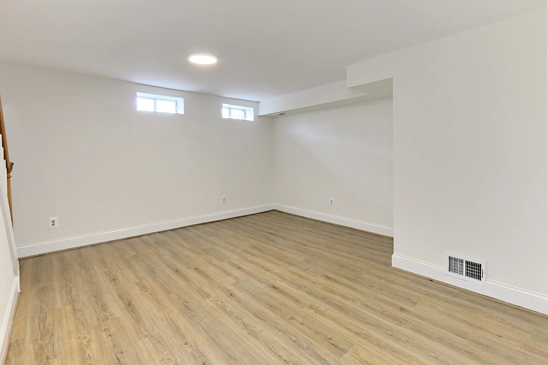 Empty room with white walls, wood flooring, three small high windows, and a ceiling light.