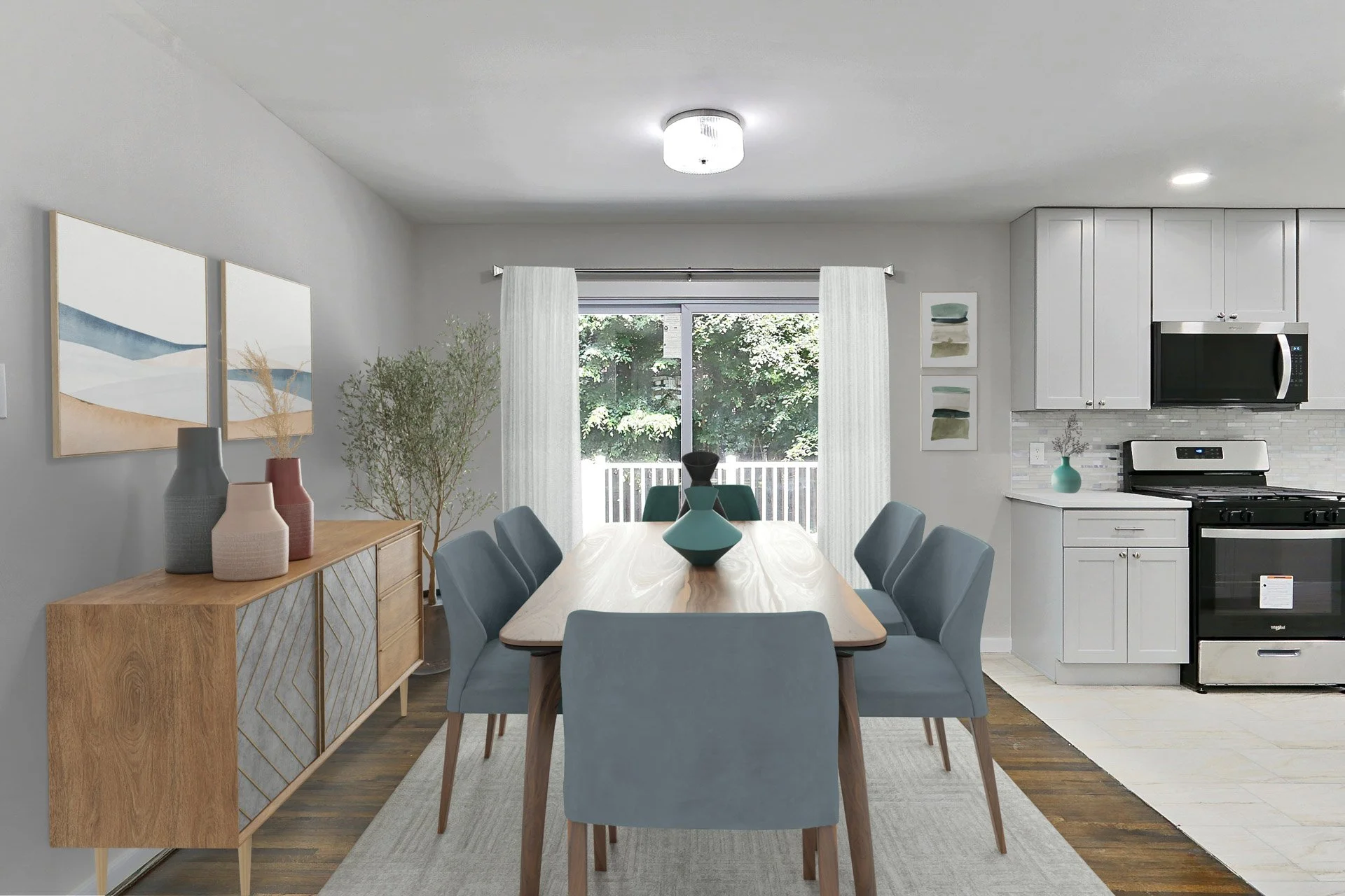 A dining area with a wooden table and eight blue chairs, a sideboard with vases, a large window with curtains, decorative artwork, and a kitchen with white cabinets and appliances in the background.