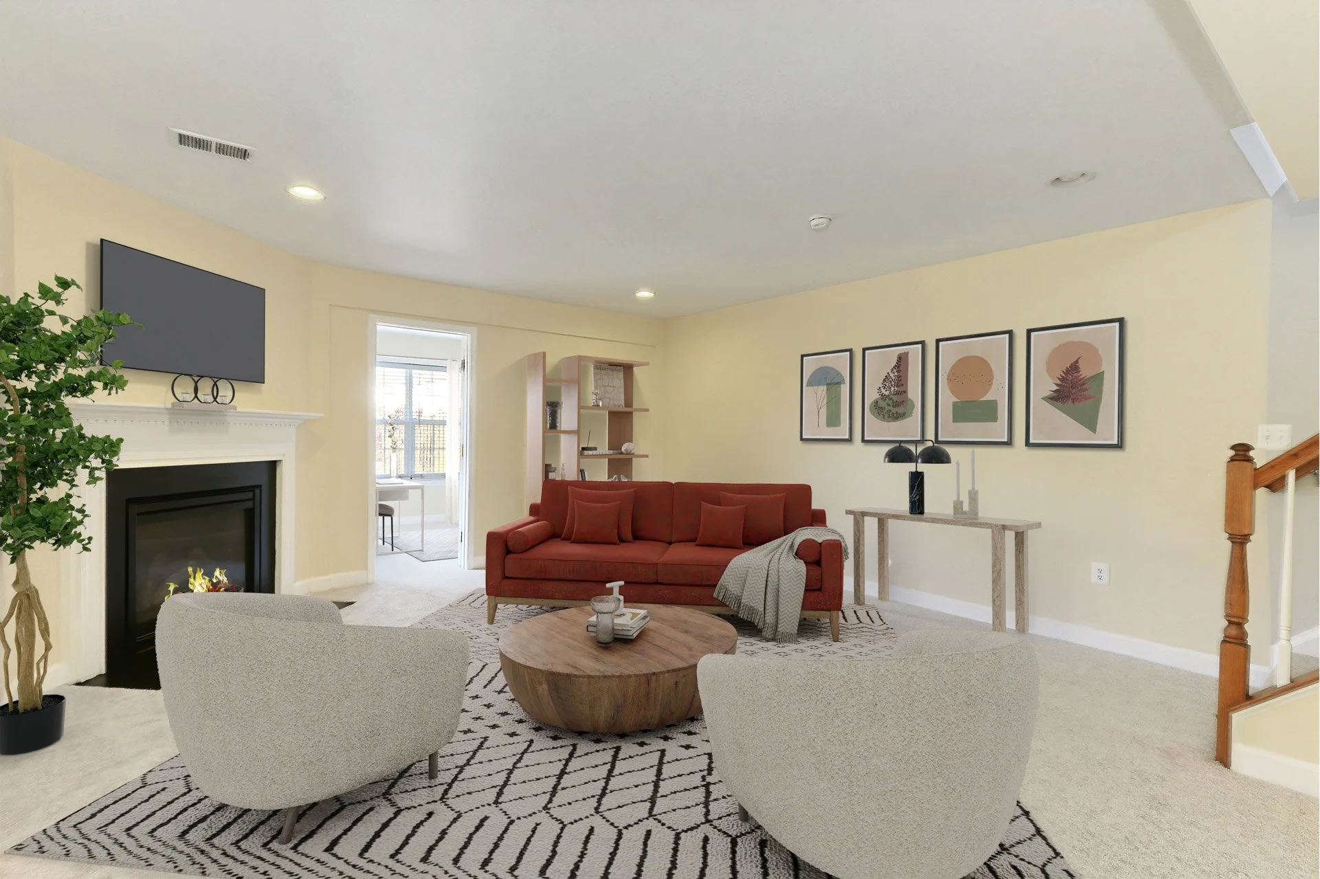 Living room with beige walls, a gas fireplace, a wall-mounted TV, a red sofa with cushions, two light gray armchairs, a round wooden coffee table, a patterned rug, artwork on the wall, a console table with decorative items, and a door leading to a su