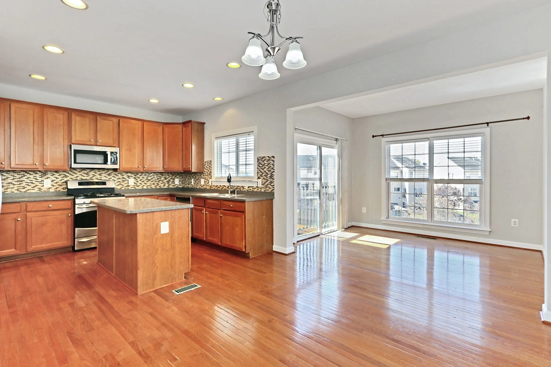 Open concept kitchen with wooden cabinets, granite countertops, and stainless steel appliances. Adjacent dining area with large windows and sliding glass door leading to balcony, hardwood floors throughout.