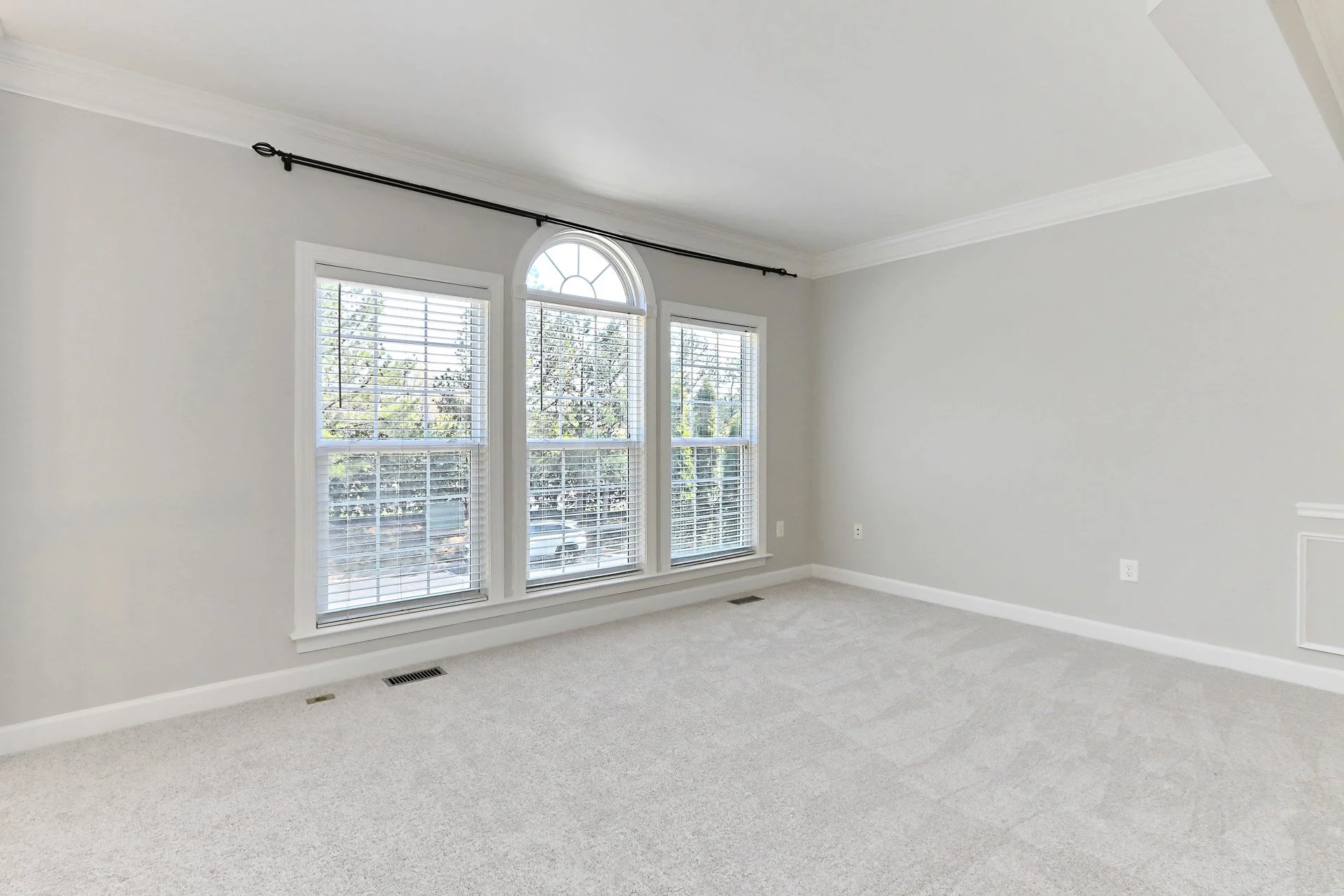 Empty room with three large windows, white walls, light carpet, and crown molding.