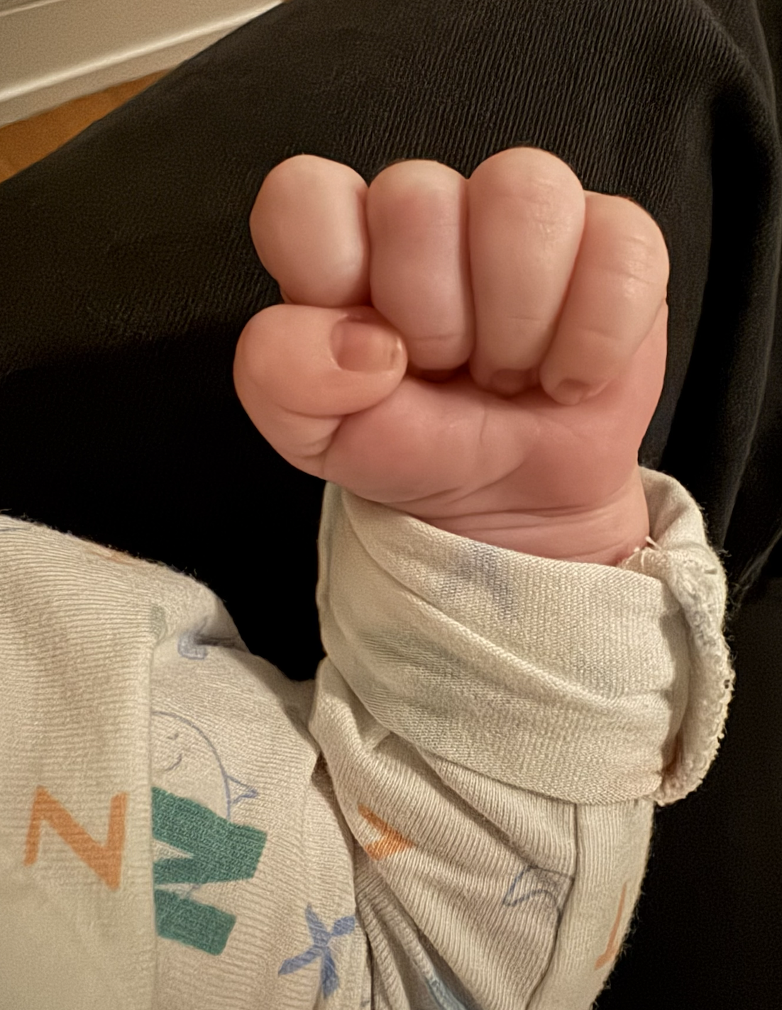 Close-up of a person's clenched fist showing the fingers curled into the palm, wearing a light-colored long sleeve shirt.