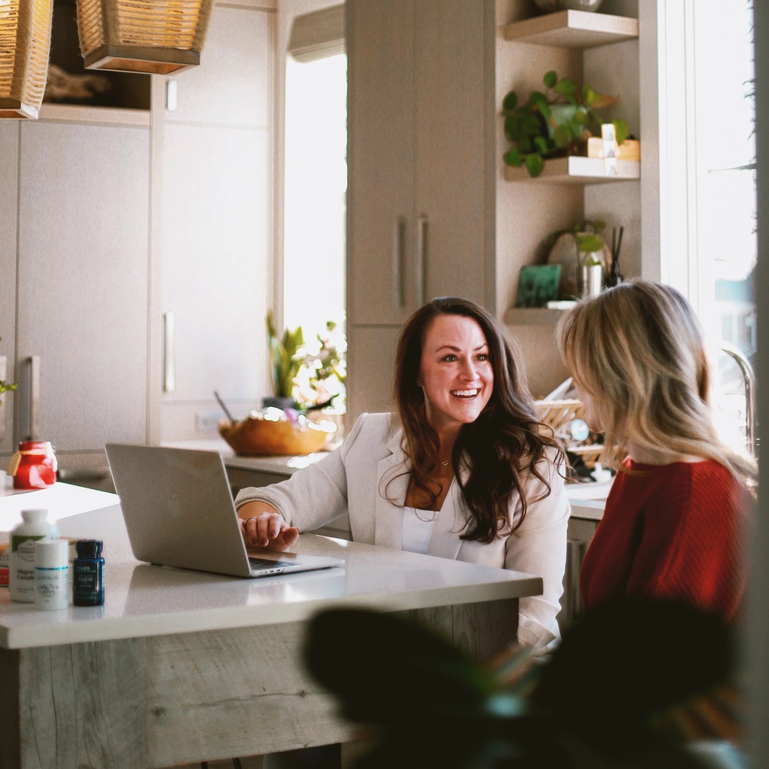 Two women working together at a computer in an office, discussing something.