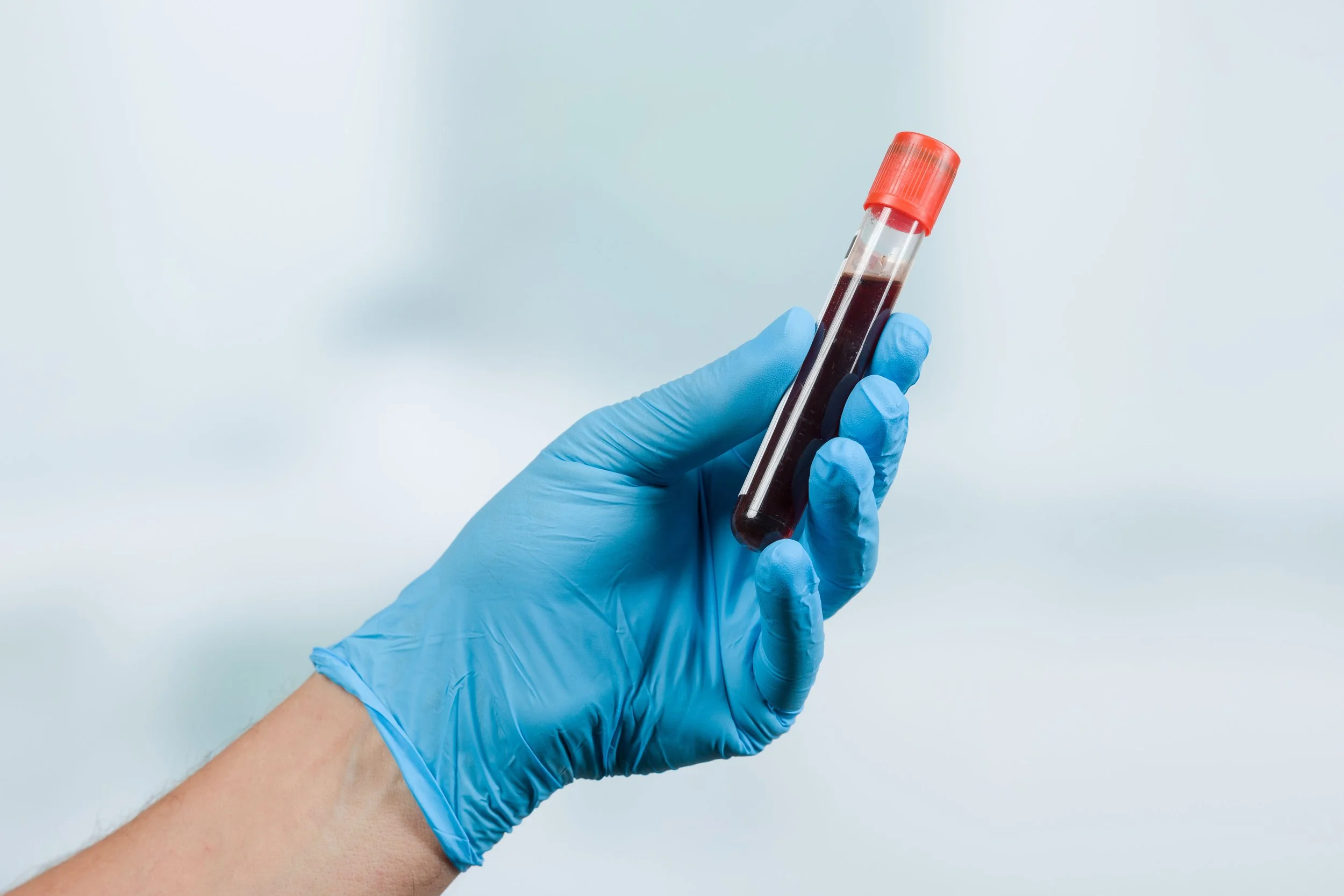 Hand in a blue glove holding a test tube filled with dark red blood.