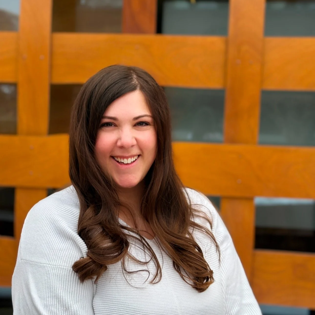 Smiling woman with long brown hair in front of a wooden lattice background.