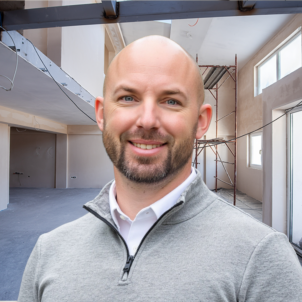 A man smiling in a room under construction with scaffolding and unfinished walls.