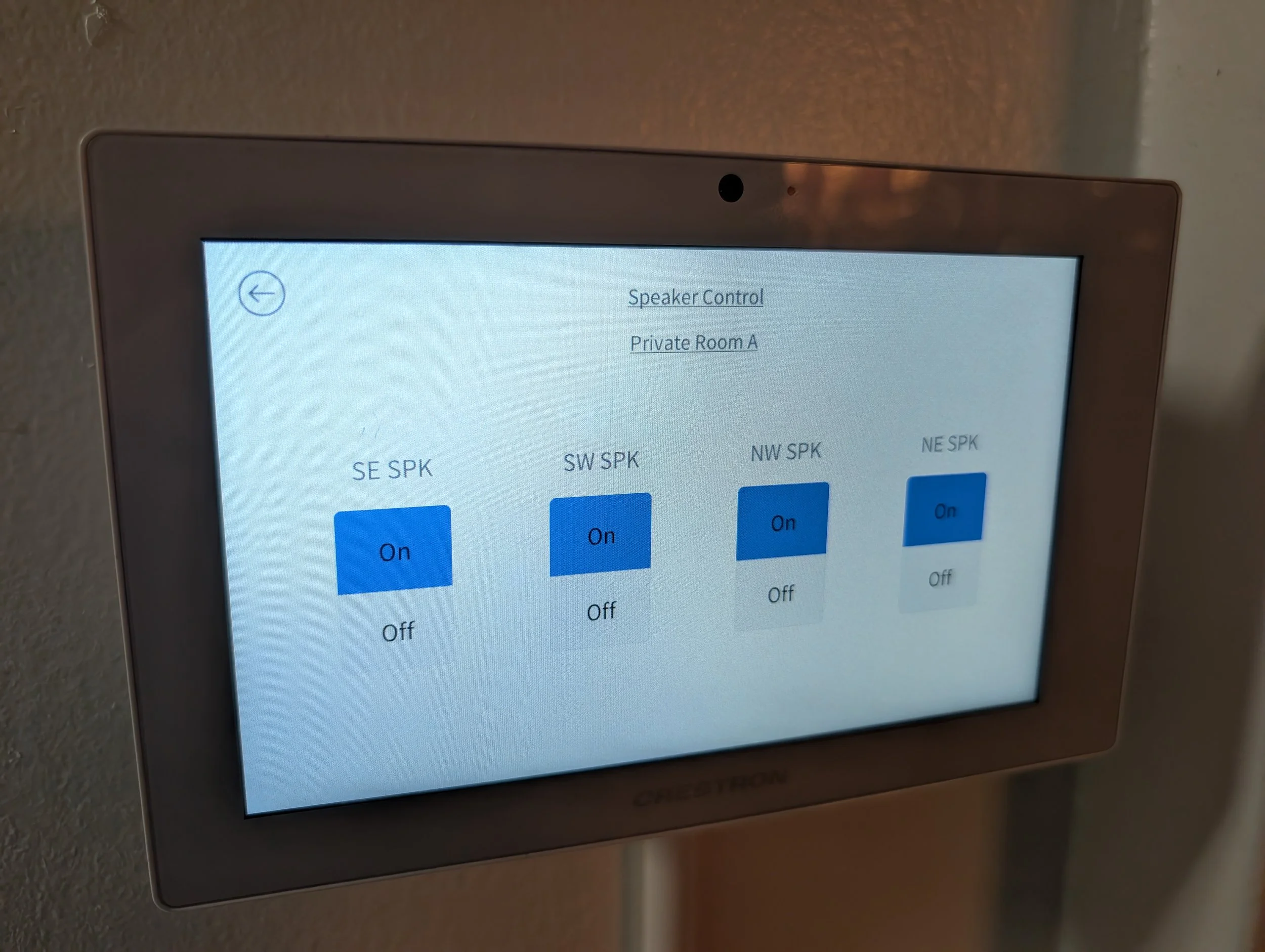 Touchscreen control panel with options to turn speakers on or off, displaying four speaker zones labeled SE SPK, SW SPK, NW SPK, and NE SPK, all set to on.