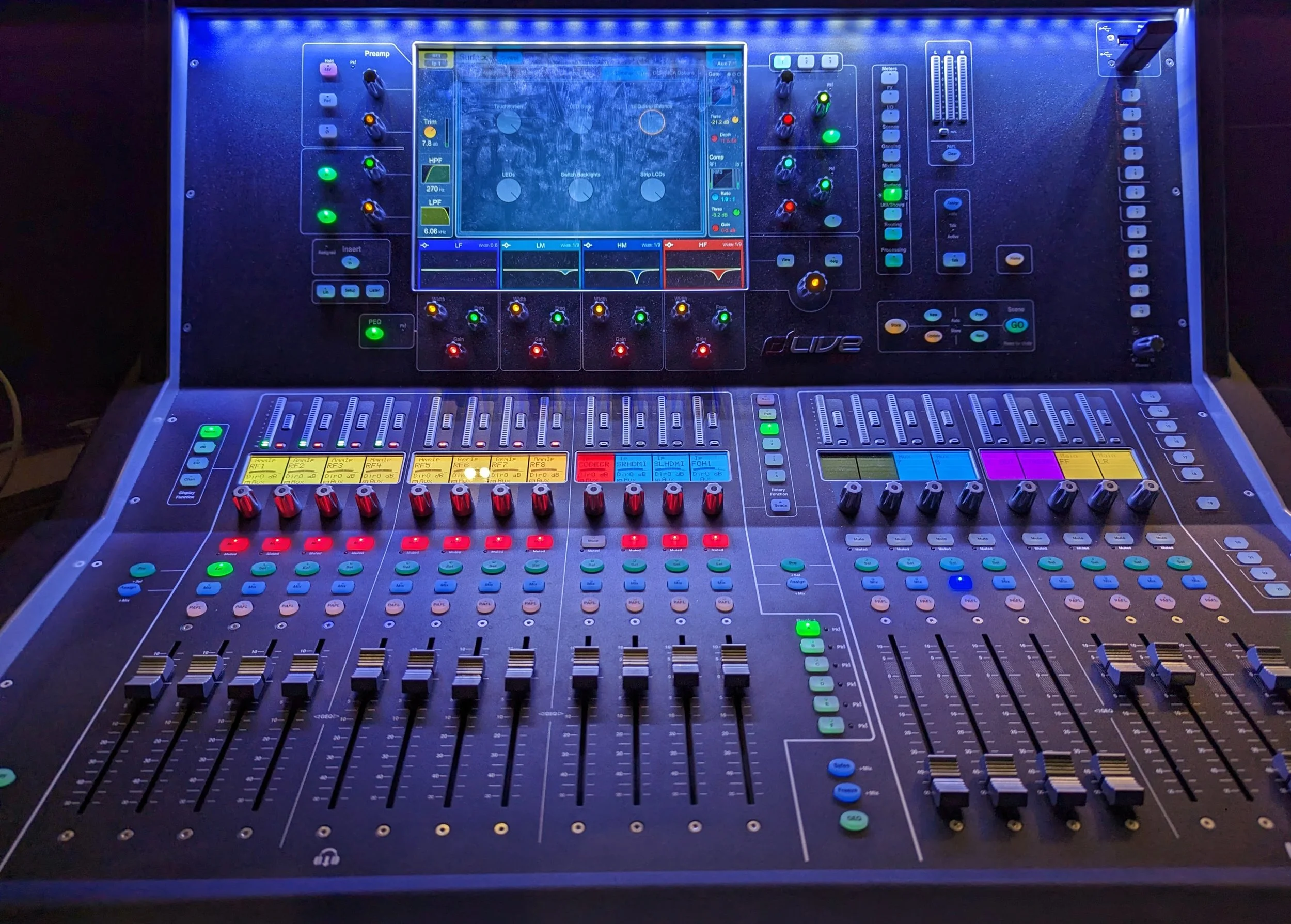 A digital audio mixing console with numerous colorful knobs, sliders, and display screens, used for sound control in audio production.