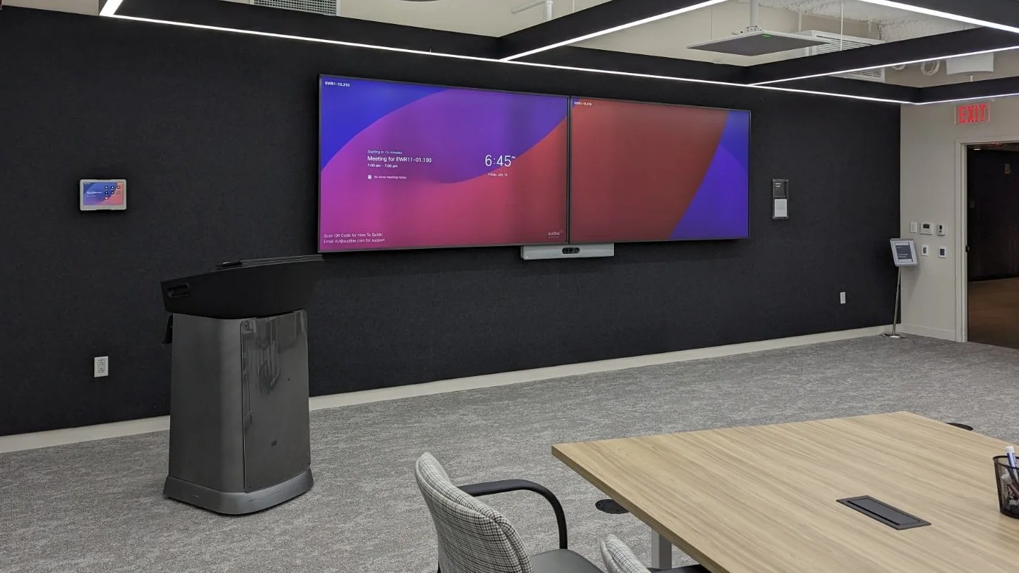 A modern conference room with a large digital screen on the wall, a podium, and a table with chairs.