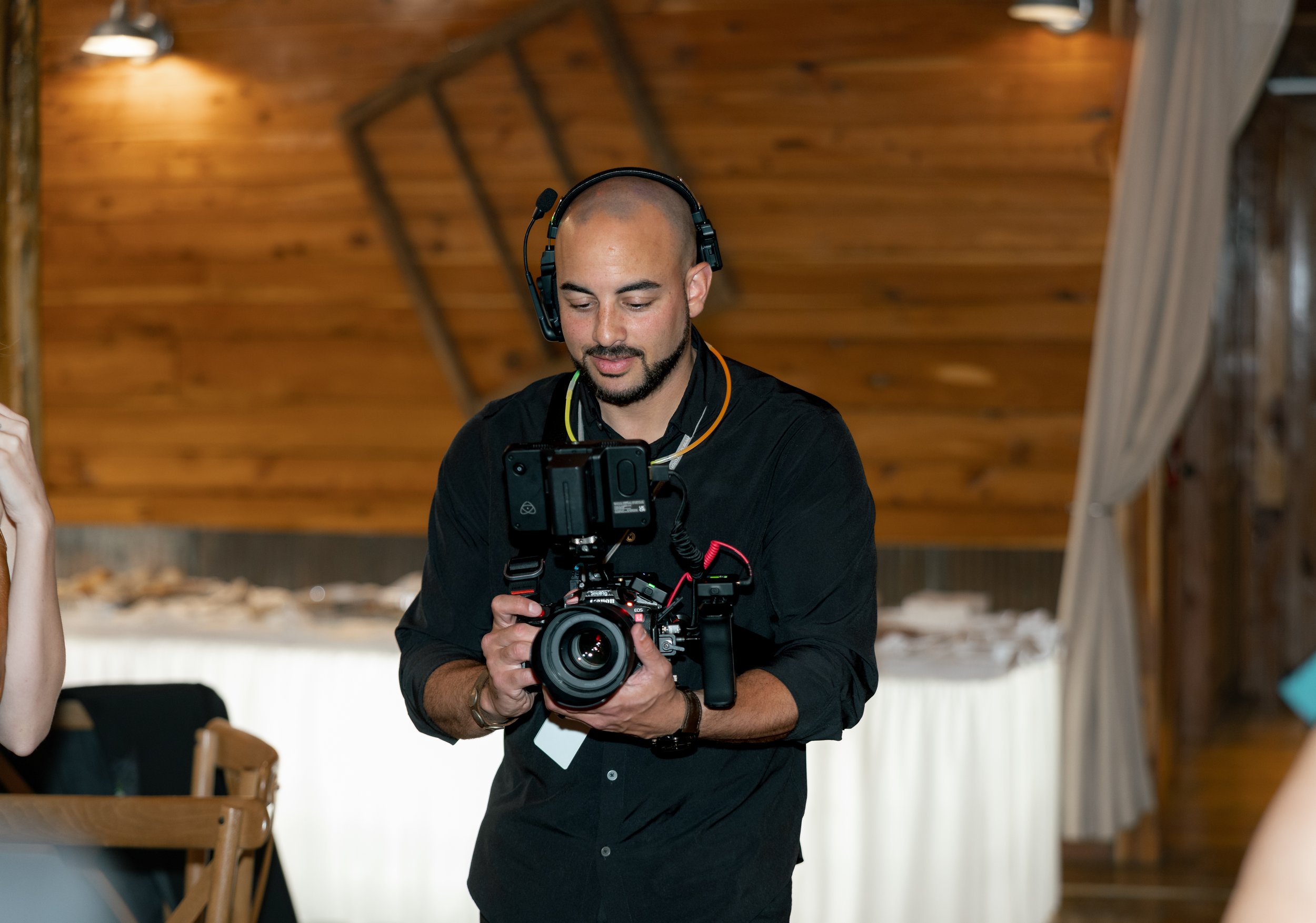 Person with headphones holding a professional camera in a wooden interior space.