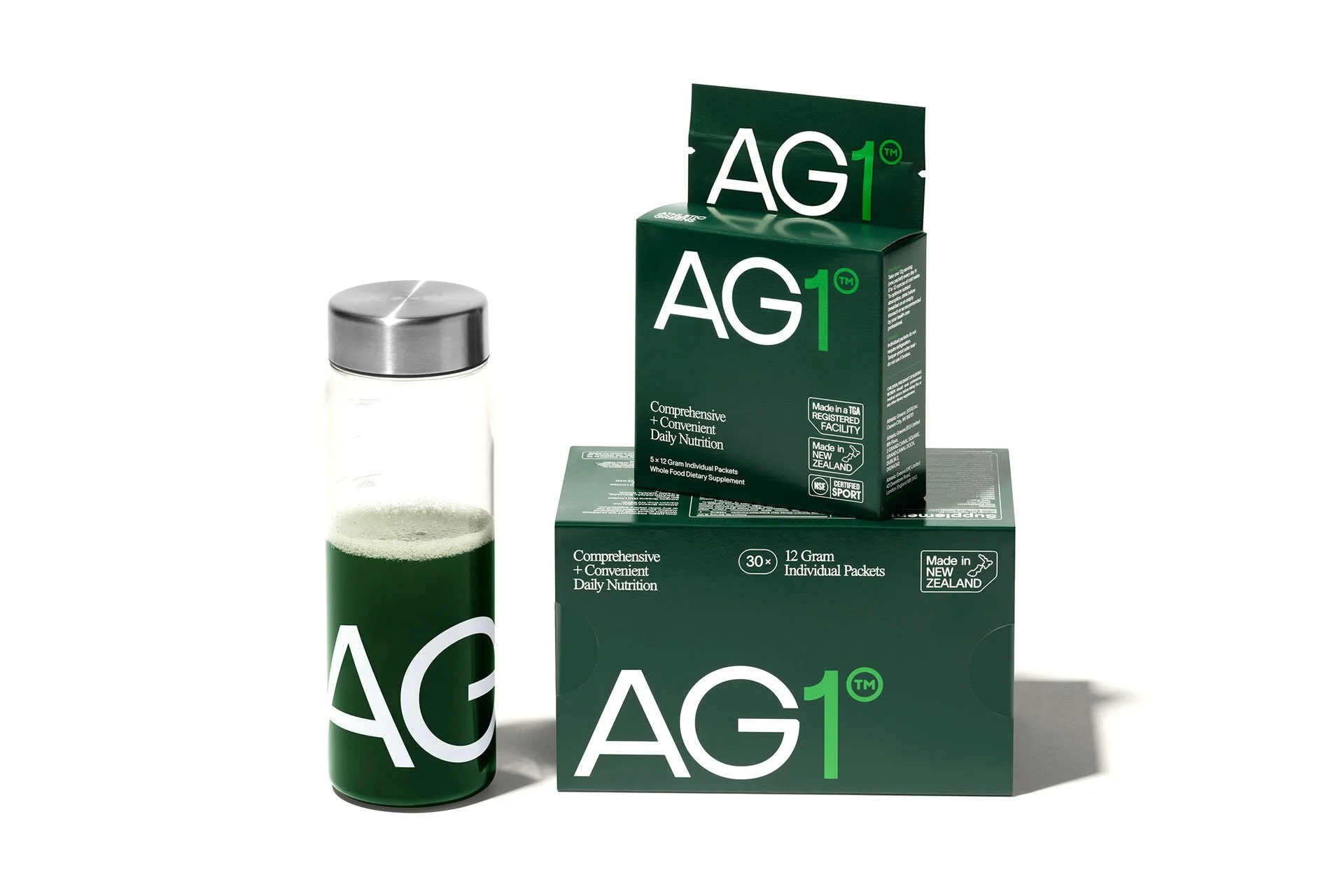 Green AG1 boxes and a branded glass bottle filled with green liquid, promoting a daily nutrition supplement.