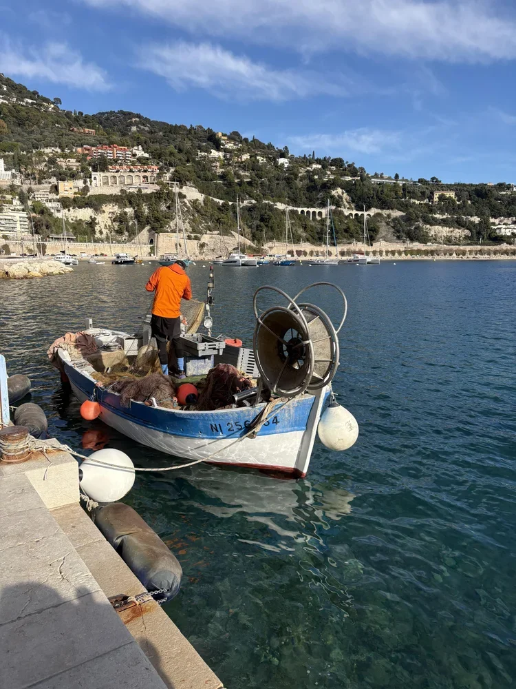 Person relaxing in black boots and jeans sitting by a fire pit at night with a red metal bench and apartment buildings in the background.