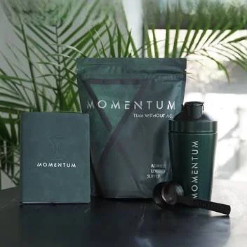 Momentum brand supplement packaging and shaker on table with leaves in background