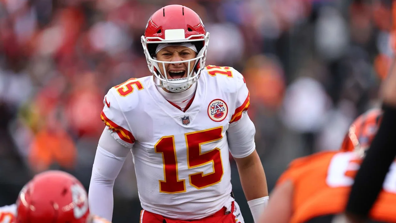 A football player wearing a white and red Kansas City Chiefs jersey with the number 15, a red helmet, and a face mask, appears to be shouting during a game.