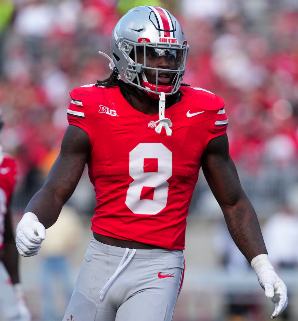 An Ohio State football player wearing a red jersey with the number 8 and a silver helmet with red and black stripes, on the field during a game.