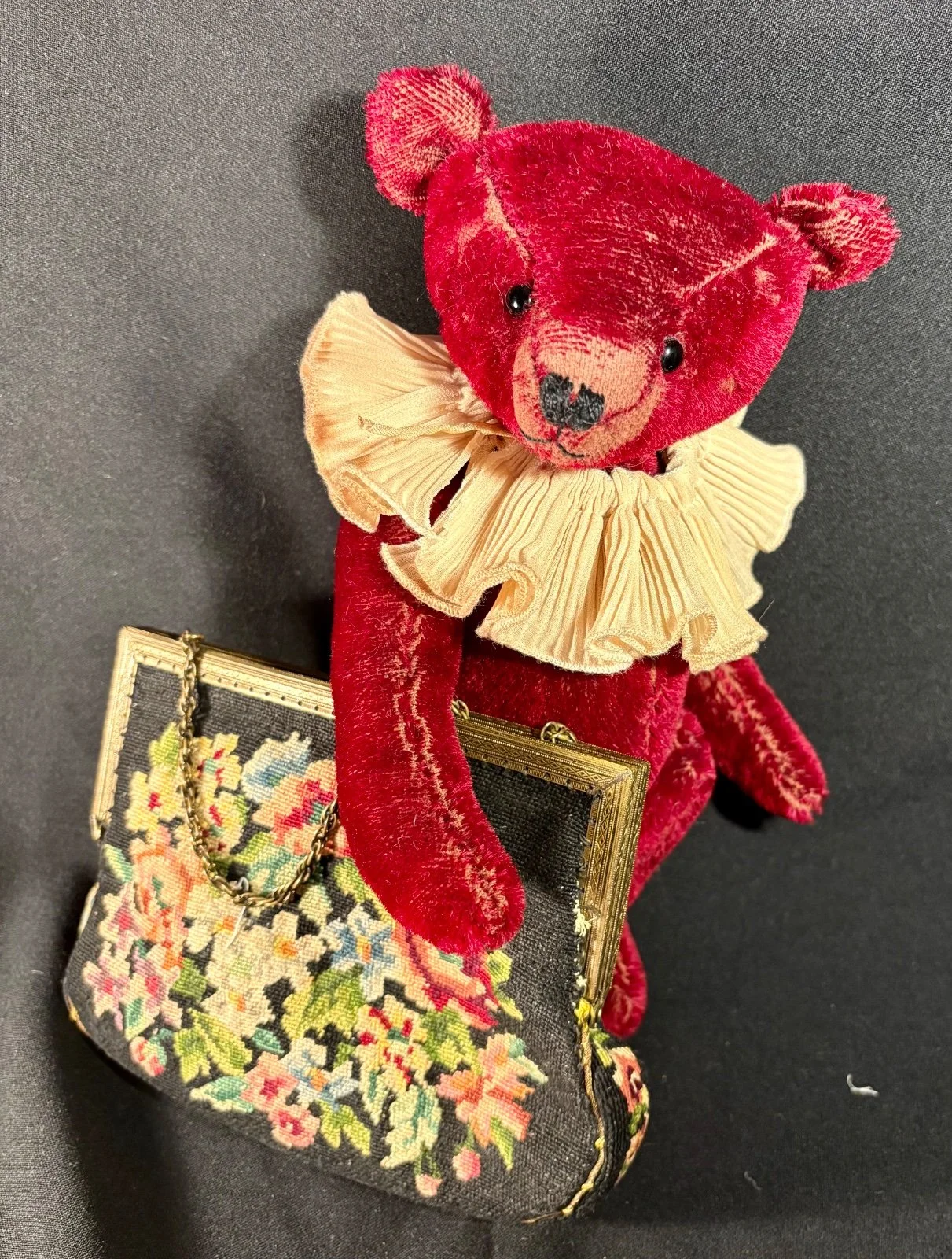 Roter Teddybär mit Rüschenkragen sitzt neben einer floralen Stofftasche, Ansicht von schräg oben
