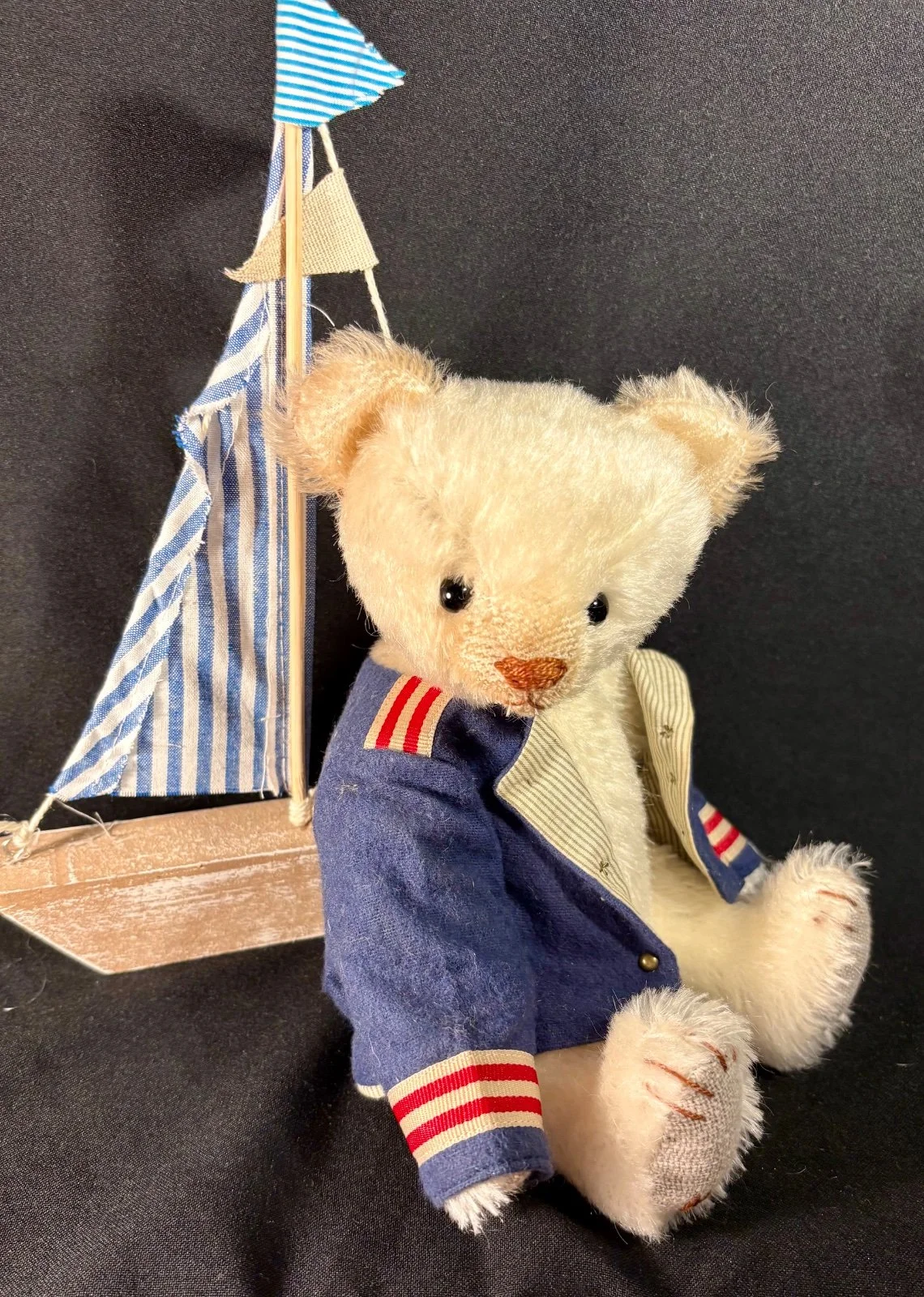 Teddybär Lars seitlich sitzend, Blick auf Segelboot mit gestreiftem Segel