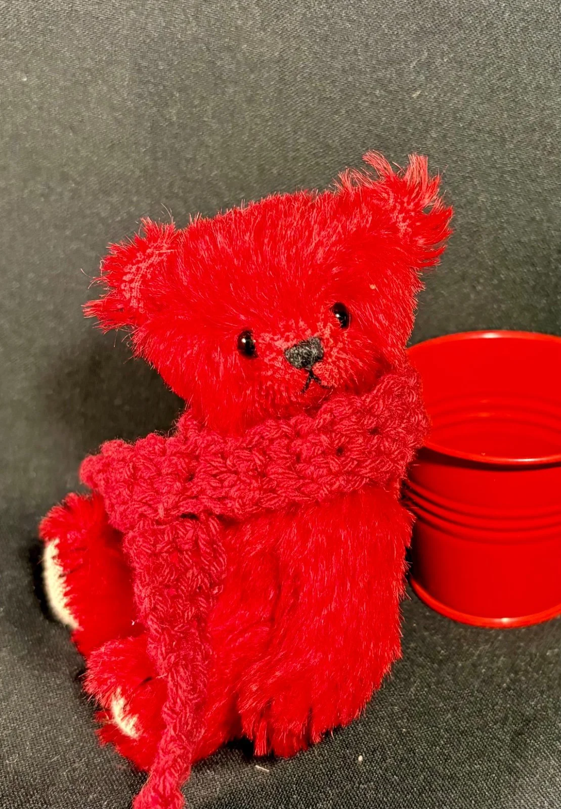 Roter Mohair-Bär mit Schal sitzt neben rotem Metalleimer, Nahaufnahme des Kopfes