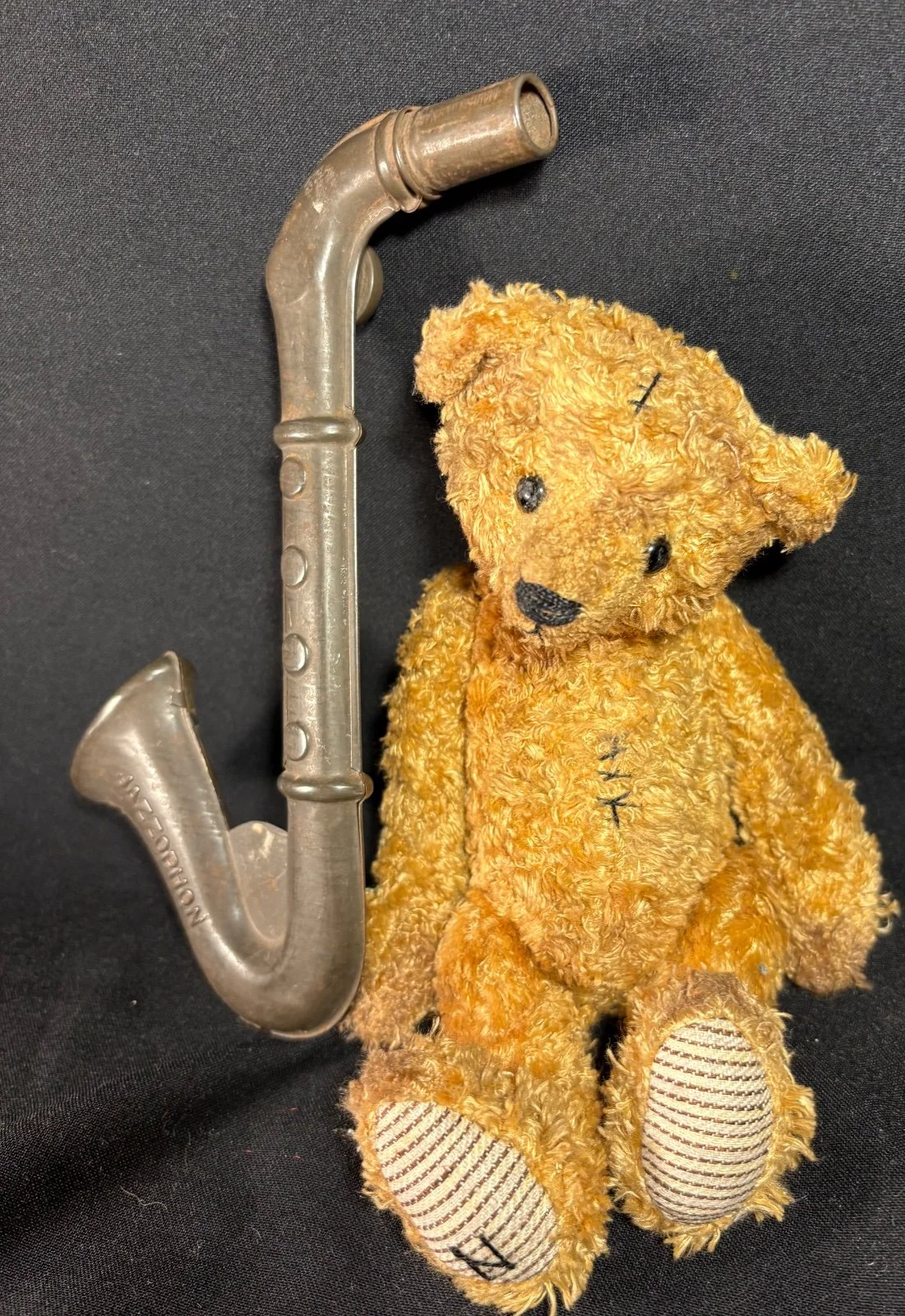 Teddybär Emil sitzend, Nahaufnahme von Kopf und Oberkörper mit sichtbaren Nähten, Spielzeug-Saxophon links im Bild