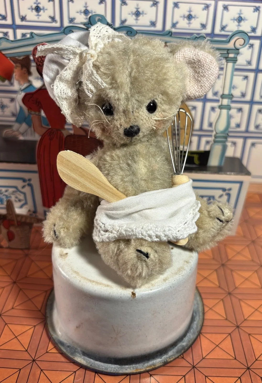 Murkel von vorn im Töpfchen sitzend, mit Haube, Schürze, Schneebesen und Holzlöffel