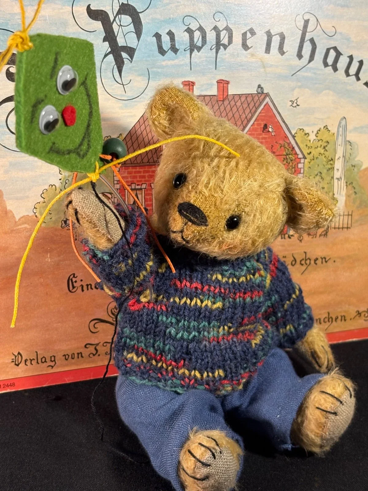 Teddybär Max von vorn sitzend, hält einen grünen Filzdrachen in der Pfote