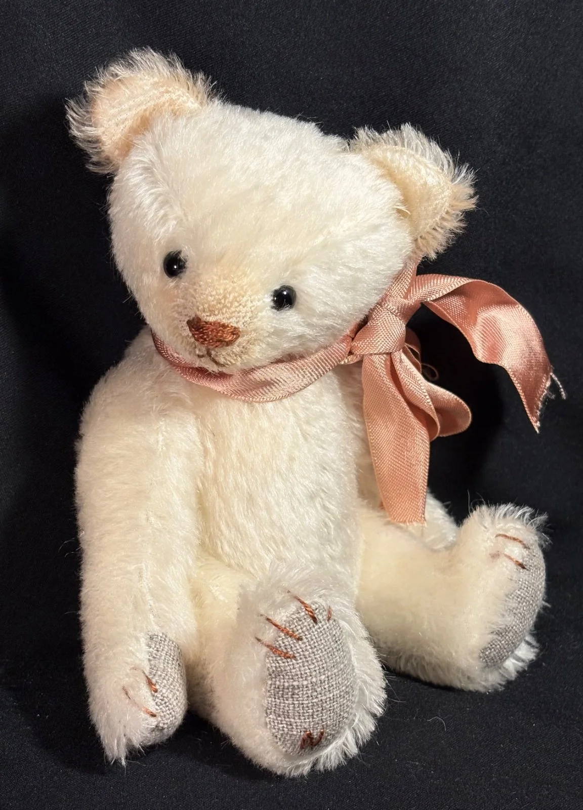 Teddybär sitzend, seitlich fotografiert, mit Blick auf Pfotensohlen und Schleife
