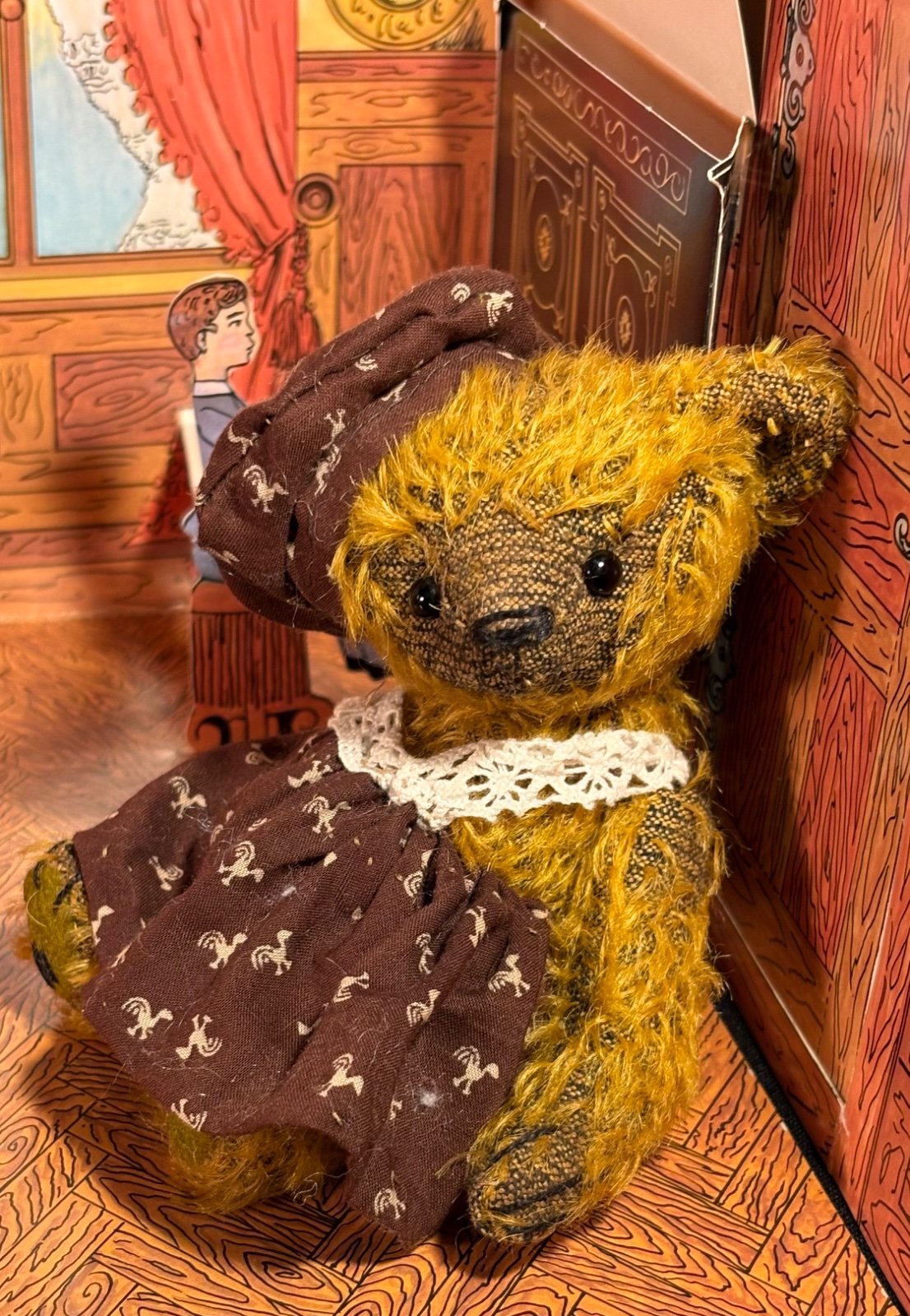 Anna von vorn sitzend, mit brauner Mütze und Kleid, vor Papiertheater-Kulisse