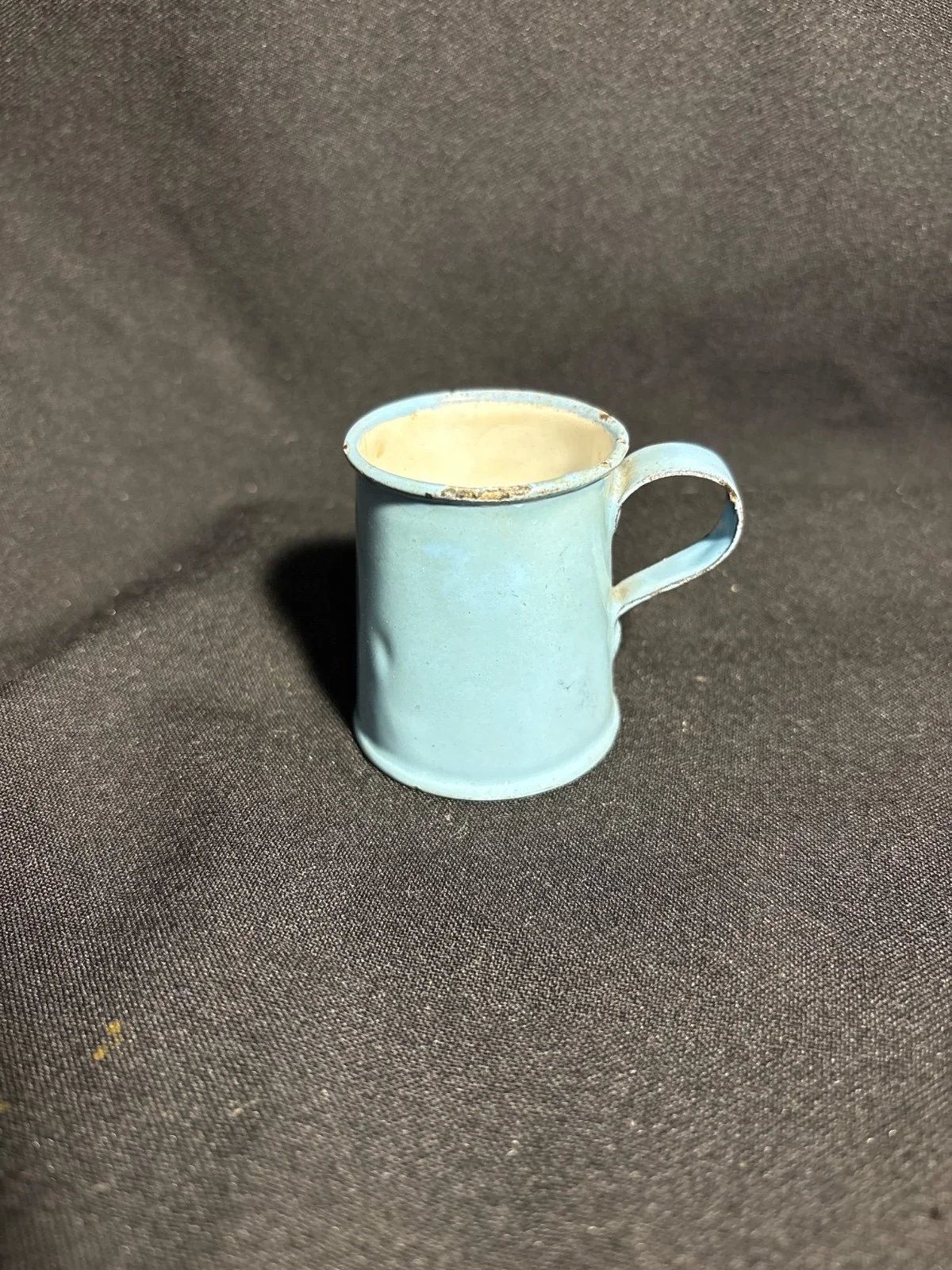 Kleines hellblaues Emaille-Töpfchen mit Henkel vor dunklem Stoffhintergrund