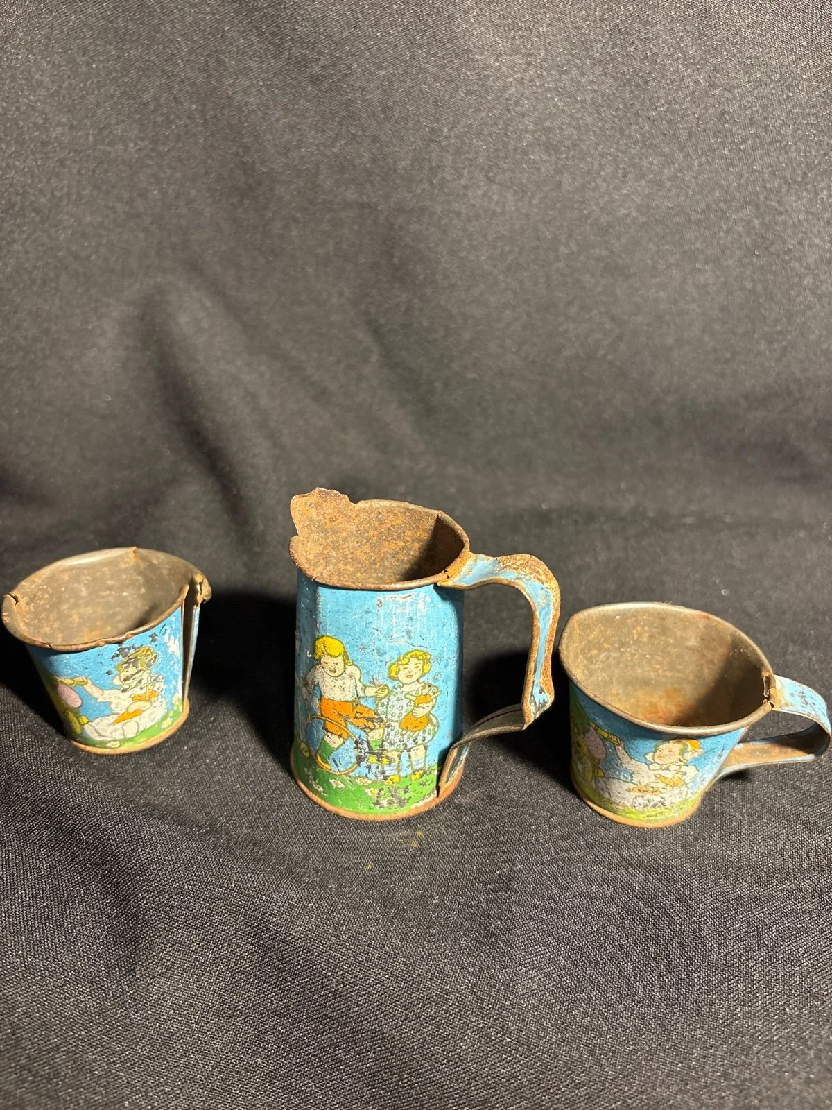 Blechkrug mit zwei Blechtassen, bemalt mit Kindermotiven, deutliche Gebrauchsspuren und Rost