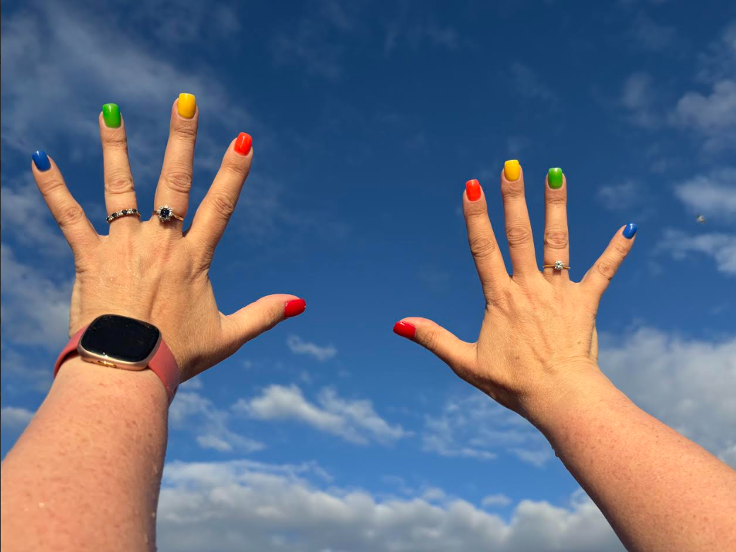 Hands with fingernails painted in Pride colours.