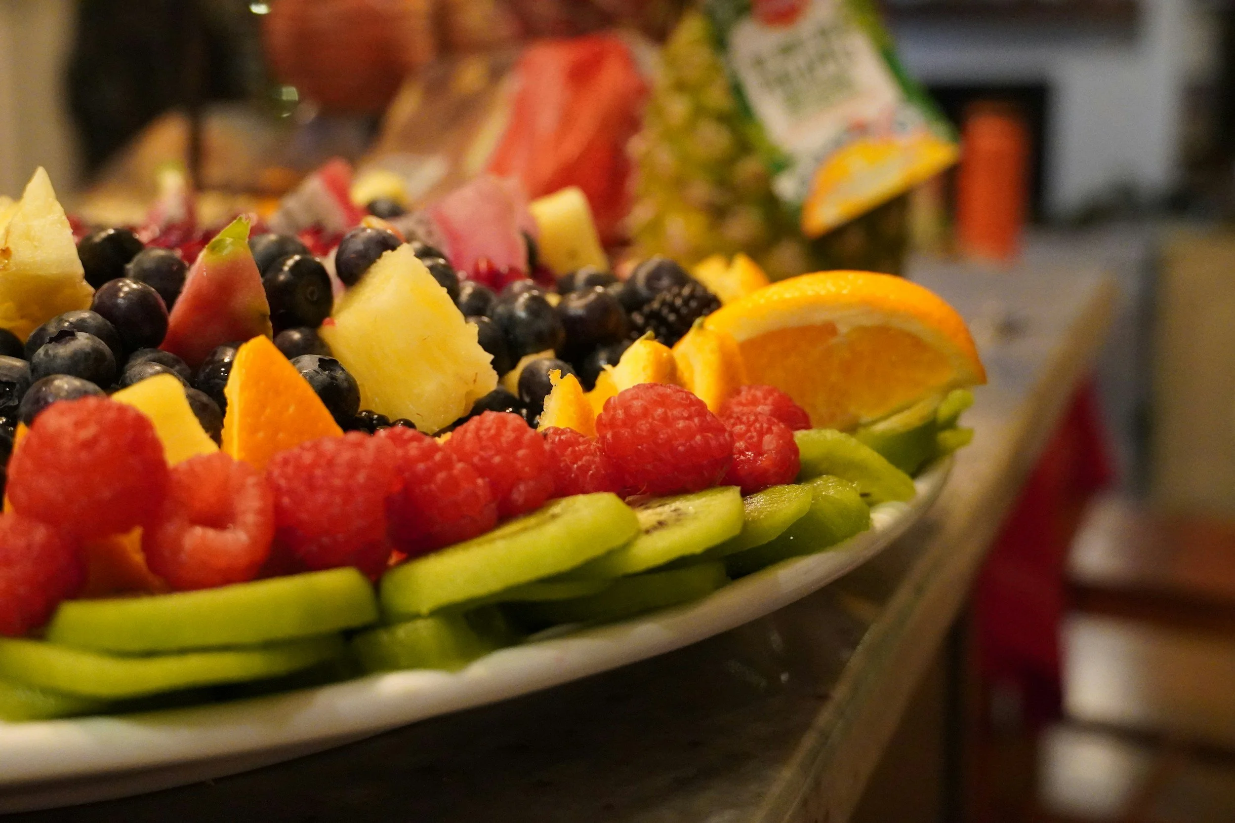 Close-up view of a large fruit platter with slices of orange, kiwi, raspberries, pineapple, grapes, and other mixed fruits arranged on a white dish.
