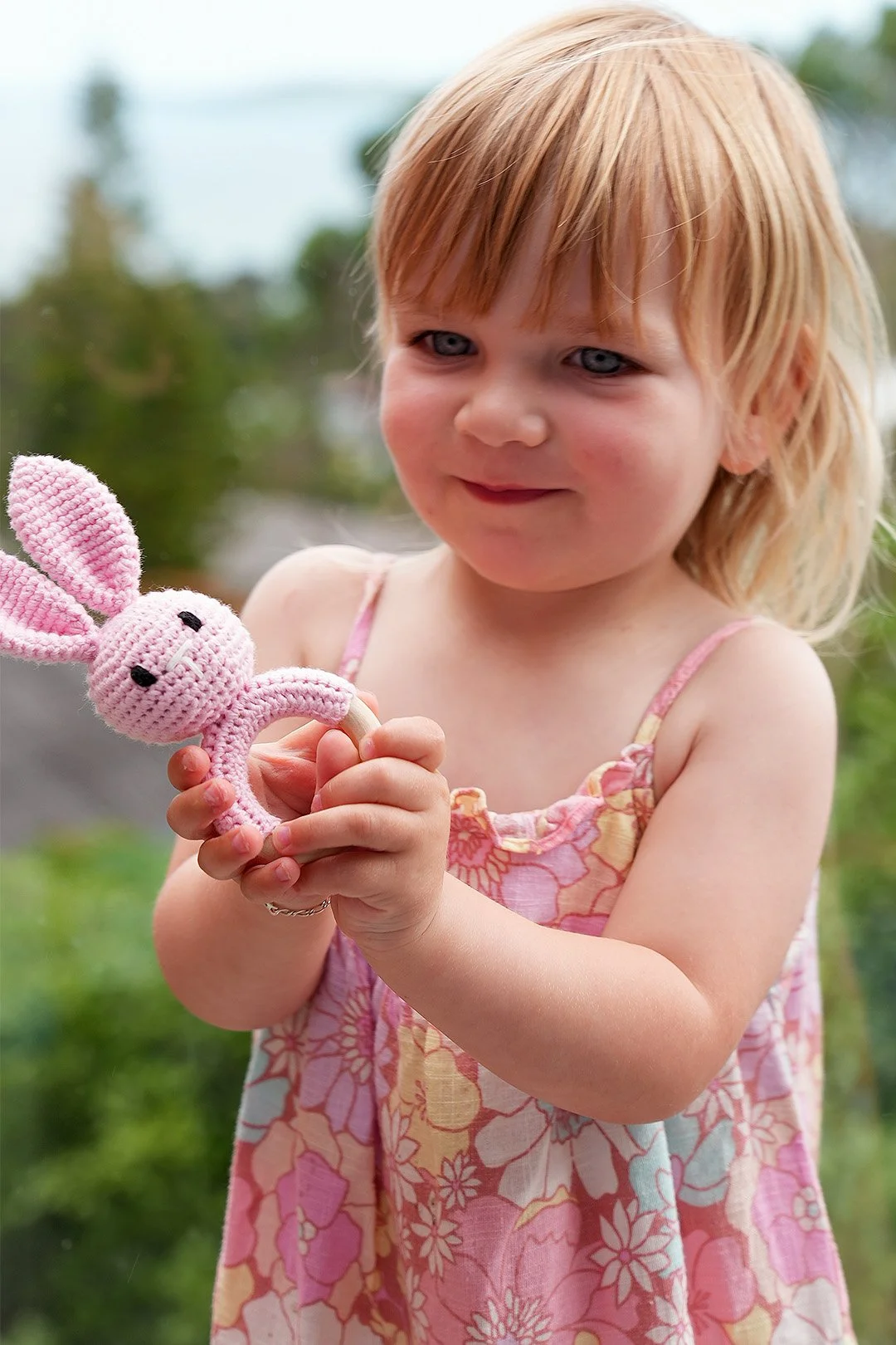 A young girl with red hair and blue eyes holding a pink crocheted bunny rattle inside a house.