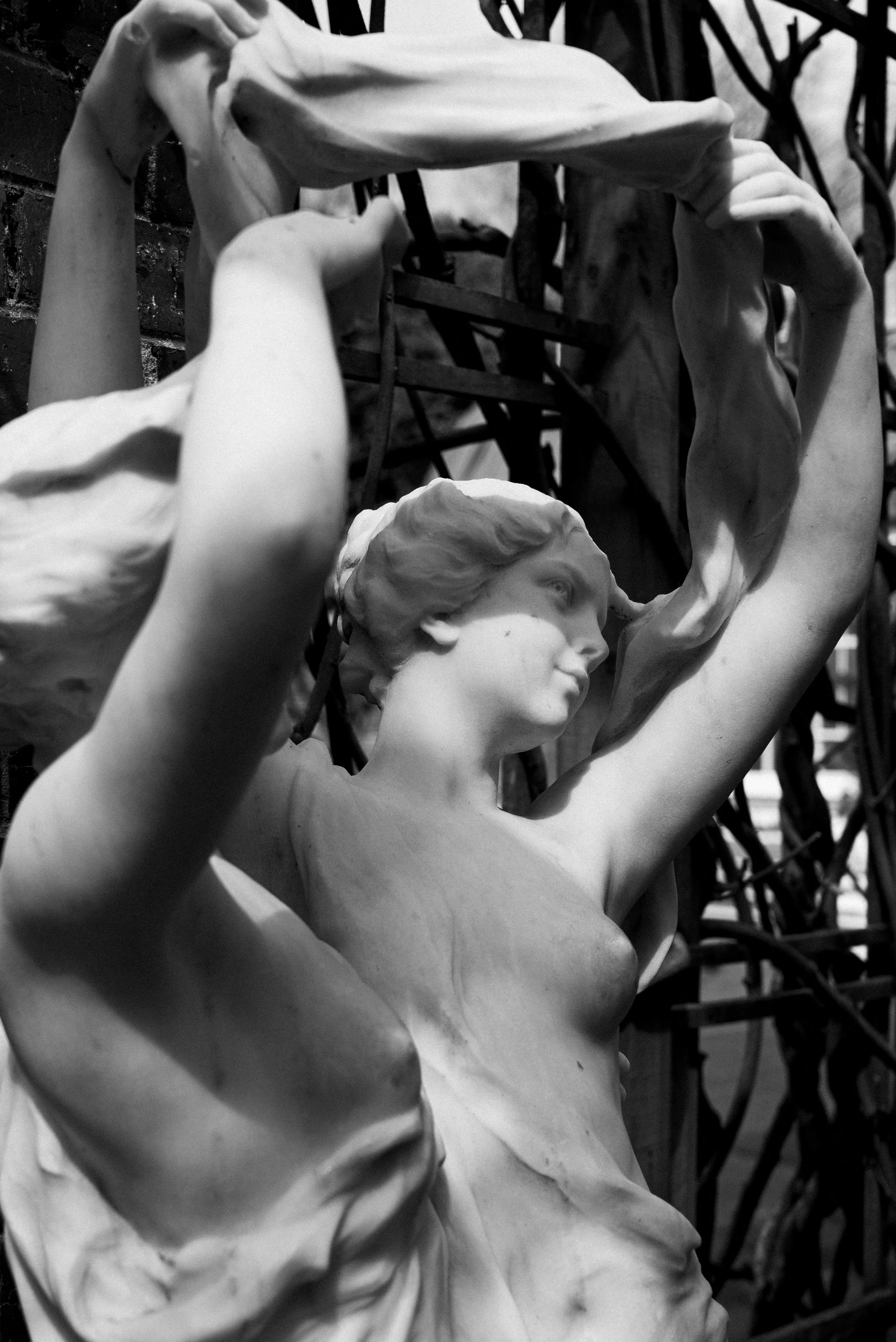 A black and white photo of classical marble sculptures of women, with one woman holding a draped fabric overhead.