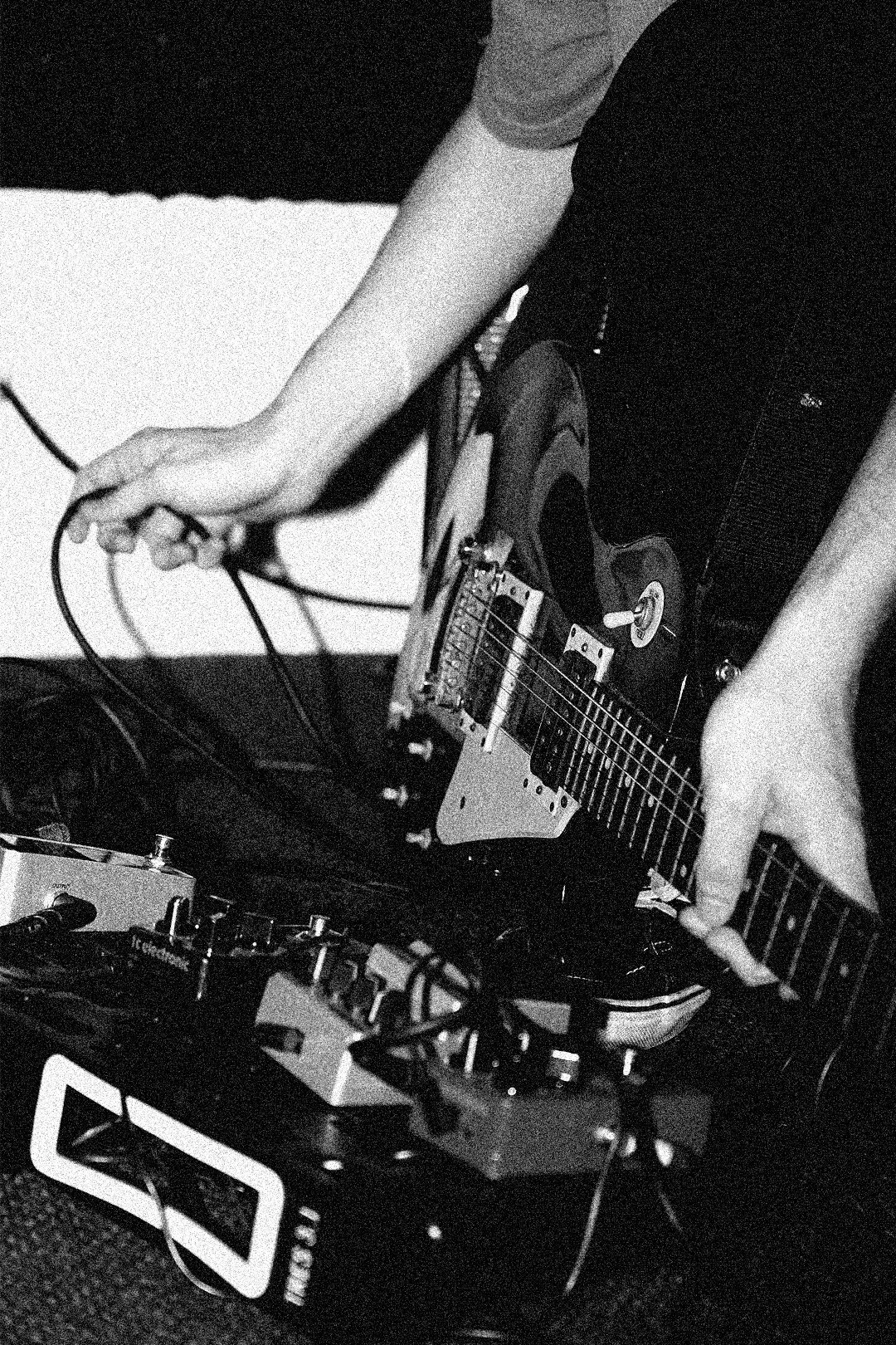 A person playing an electric guitar, with music equipment and cables visible around.