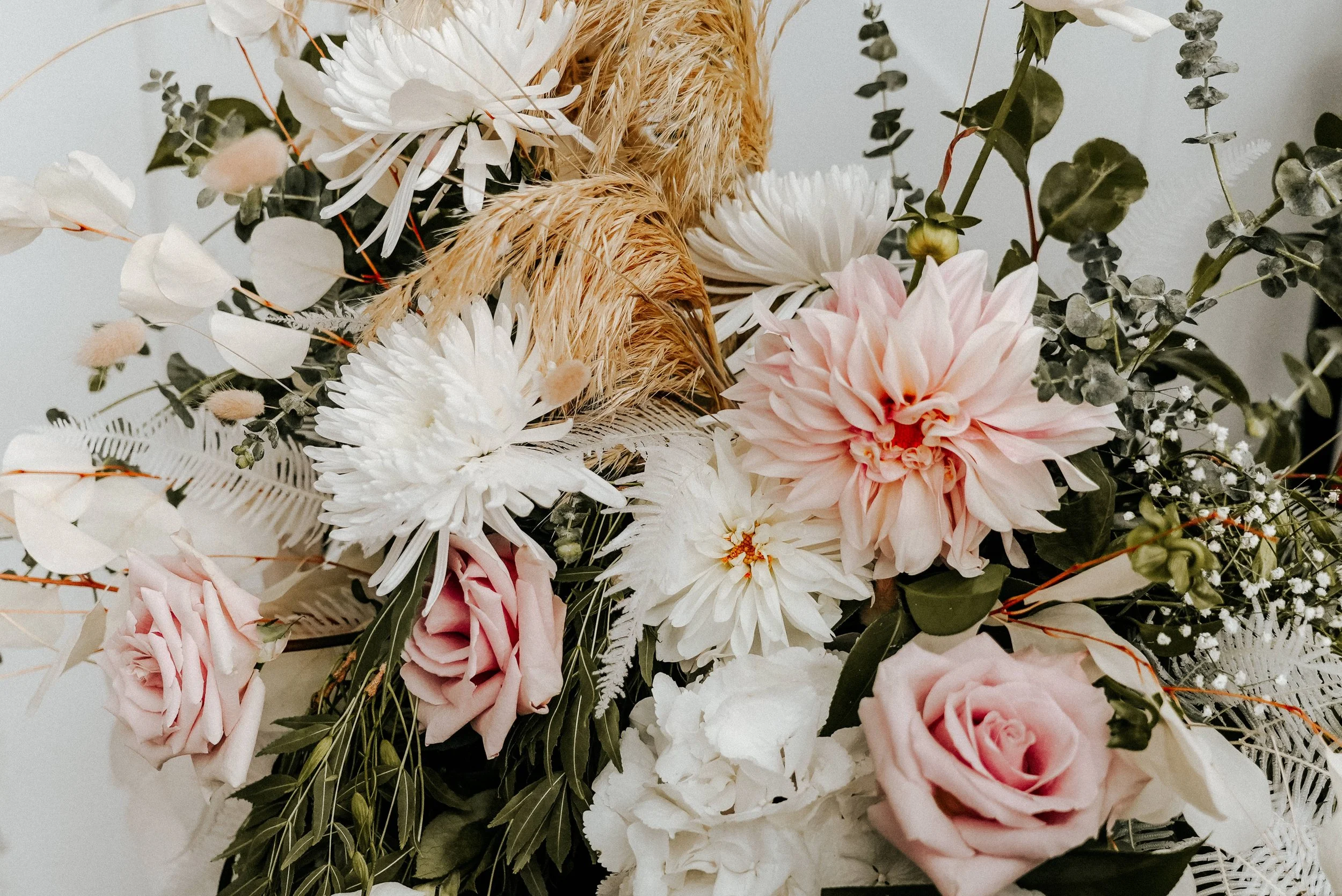Bouquet of pink and white flowers, including roses and dahlias, with greenery and dried wheat stalks.