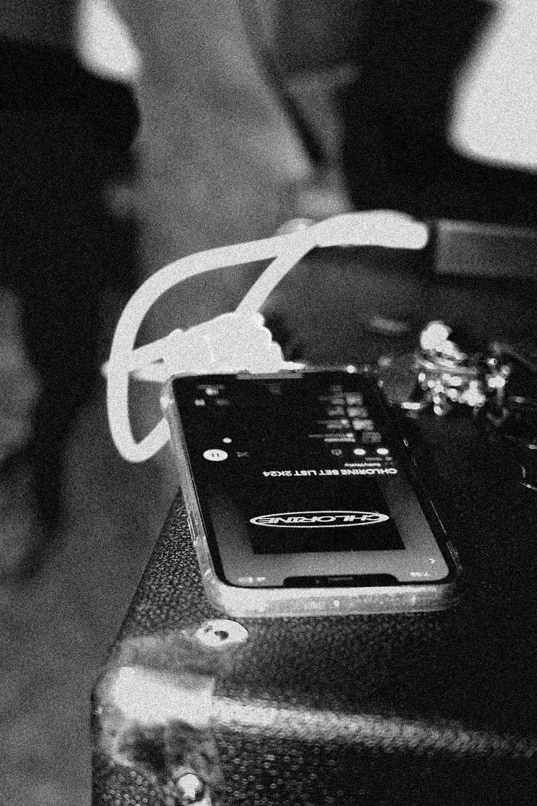 Close-up of a smartphone with a digital display, placed on a textured surface, with a white cable connected to it, and various electronic items around it.