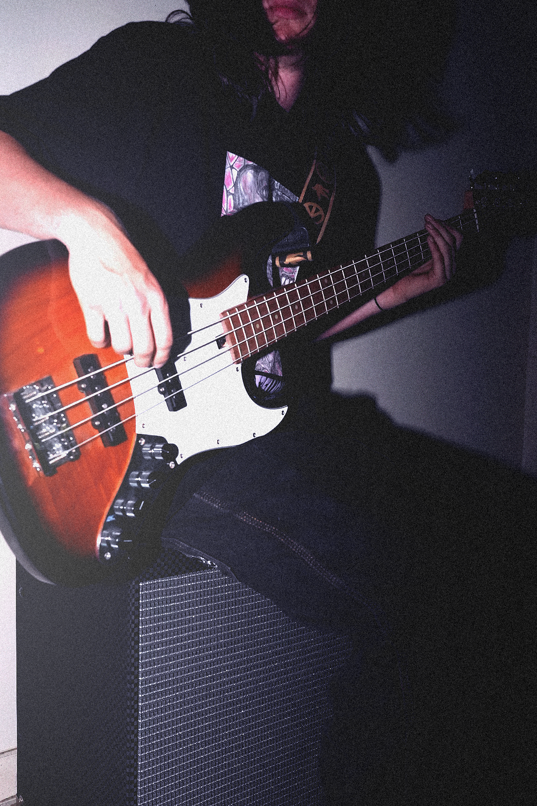 Person playing an electric bass guitar in a dimly lit room, focusing on the instrument and their hands.