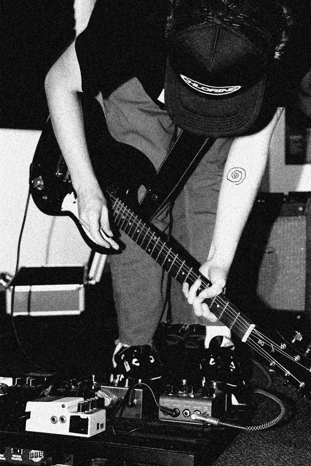 A person wearing a cap and a t-shirt playing an electric guitar surrounded by audio equipment in a music studio.