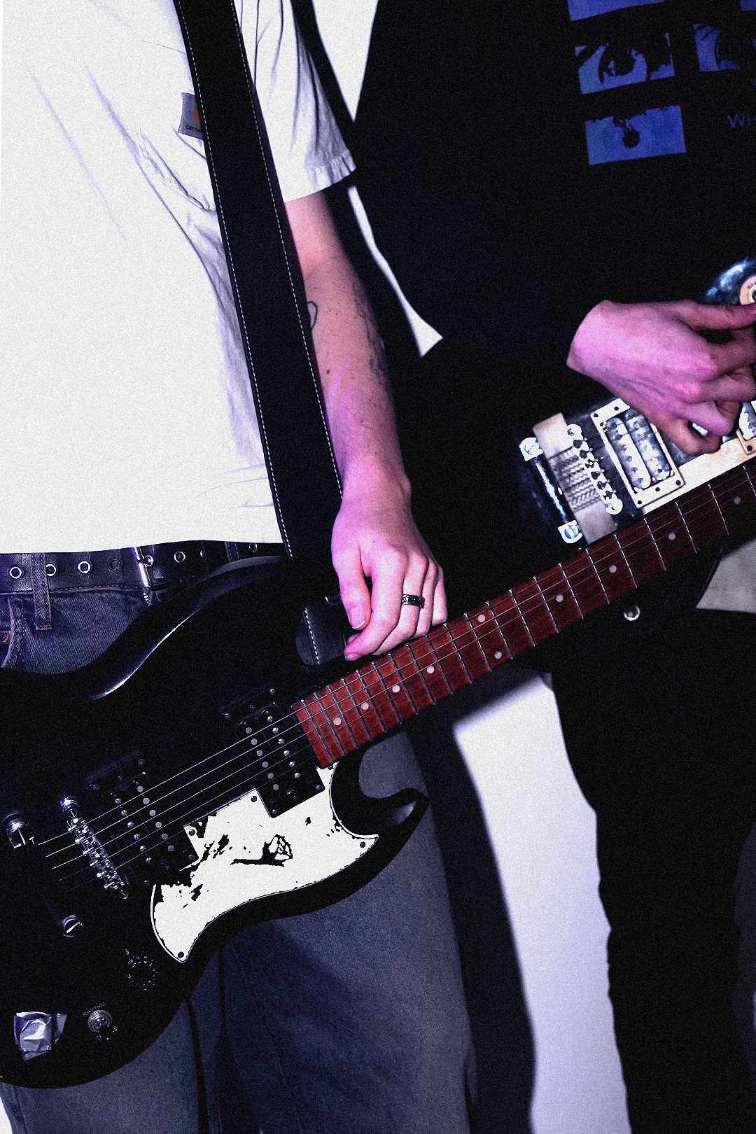 Close-up of two musicians playing electric guitars, one with a black guitar and another with a cream-colored guitar, with visible hands and part of their torsos.