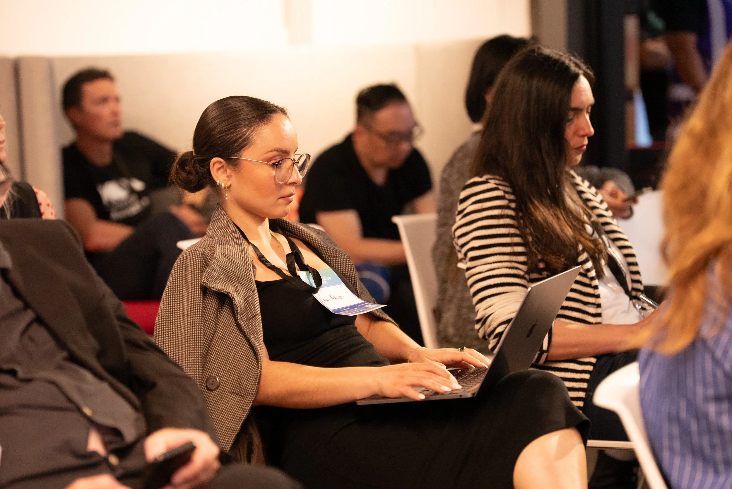 Women attending a conference, some using laptops and taking notes, in a professional setting.