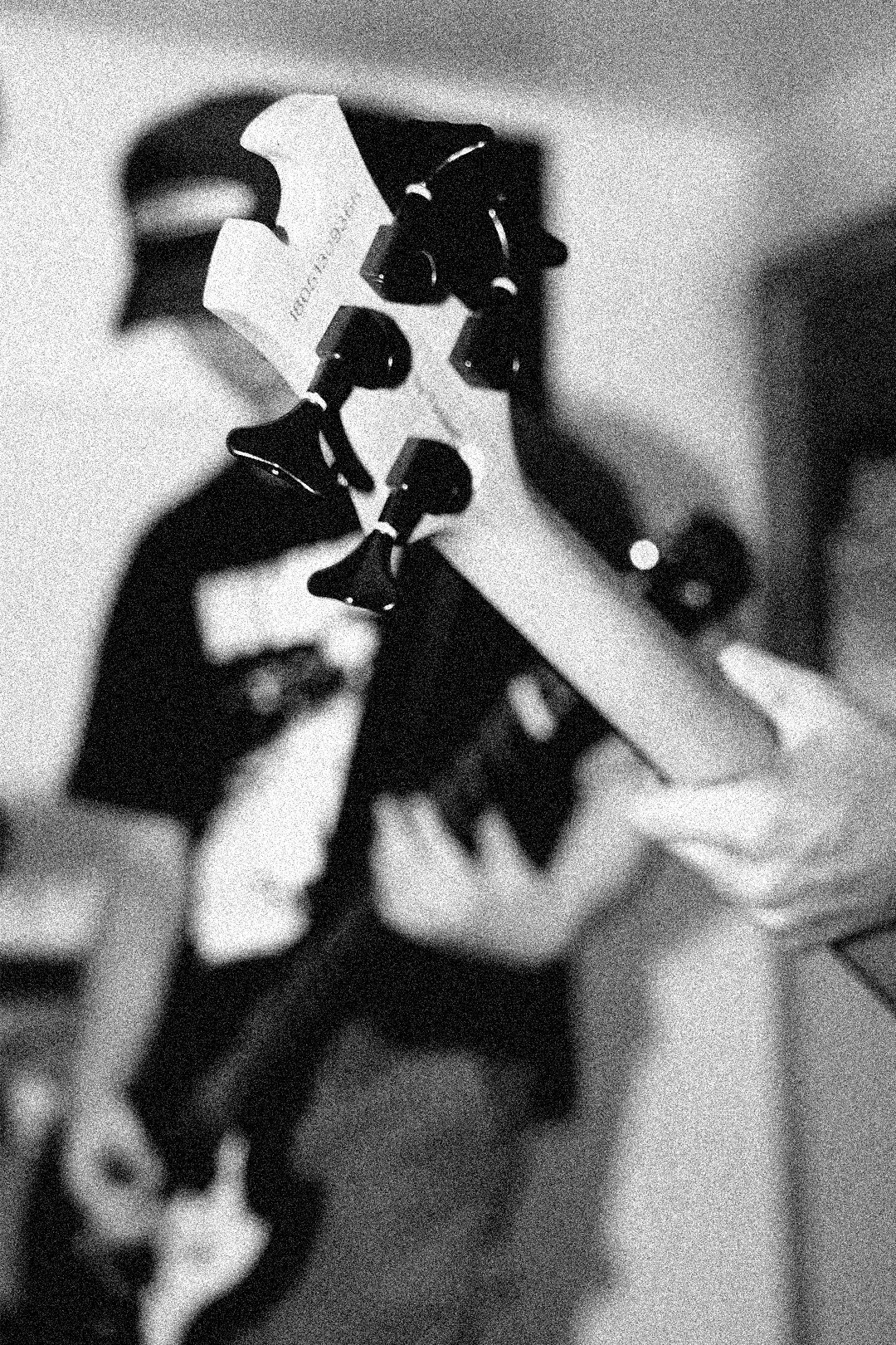 A person holding an acoustic guitar, with a focus on the headstock and tuning pegs, in black and white.