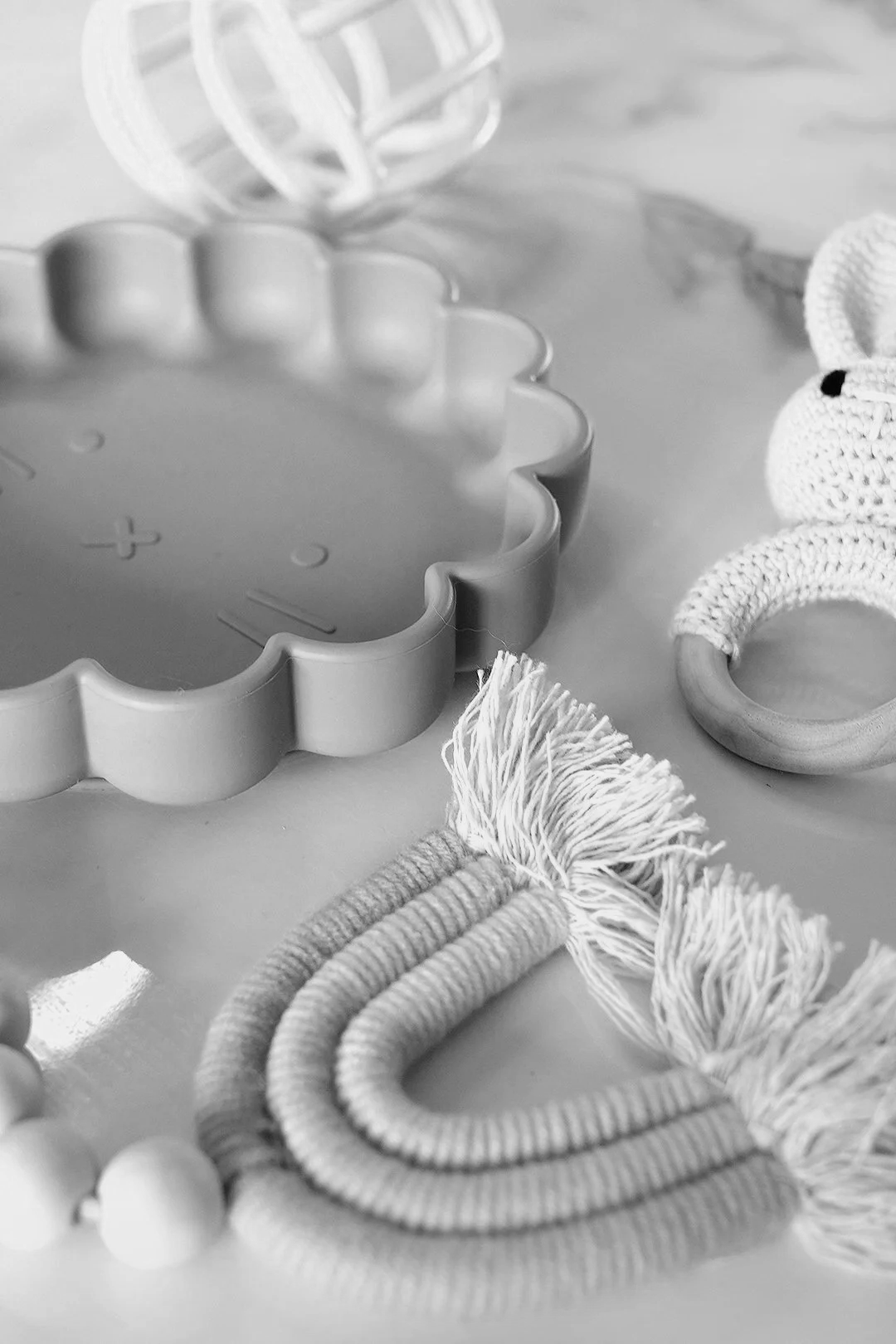 Close-up of baby toys including a teething ring, a rattle, and a cloth teddy bear on a light surface.